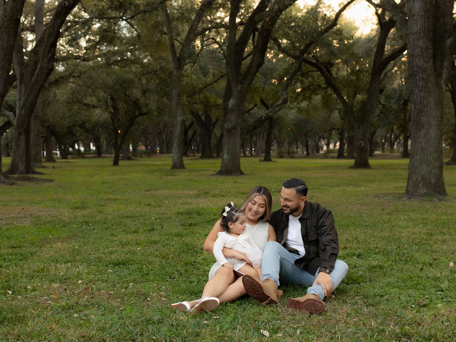 A family shares intimate moments while sitting on grass in a park setting.