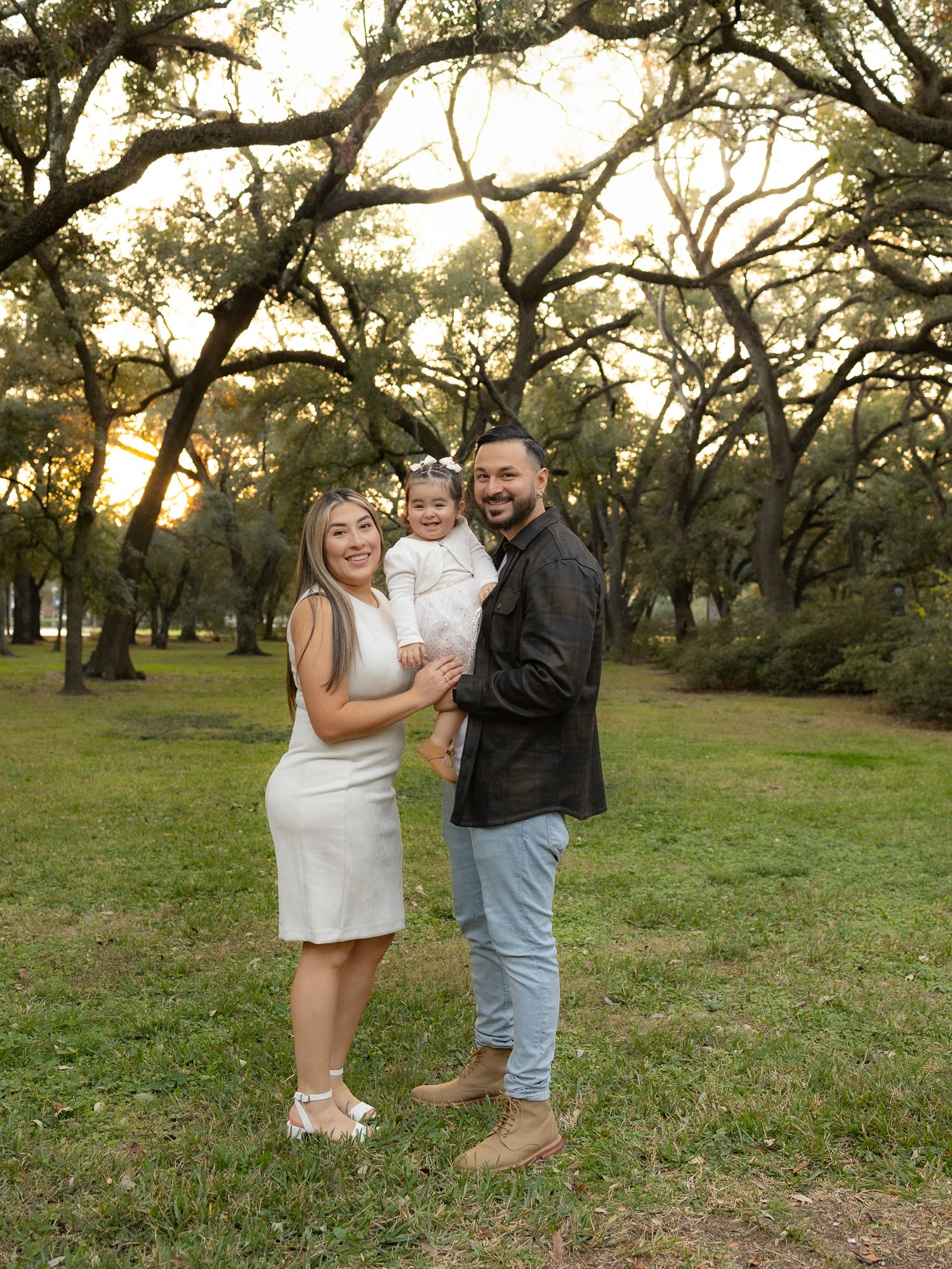 A family portrait in a park with beautiful oak trees during golden hour.