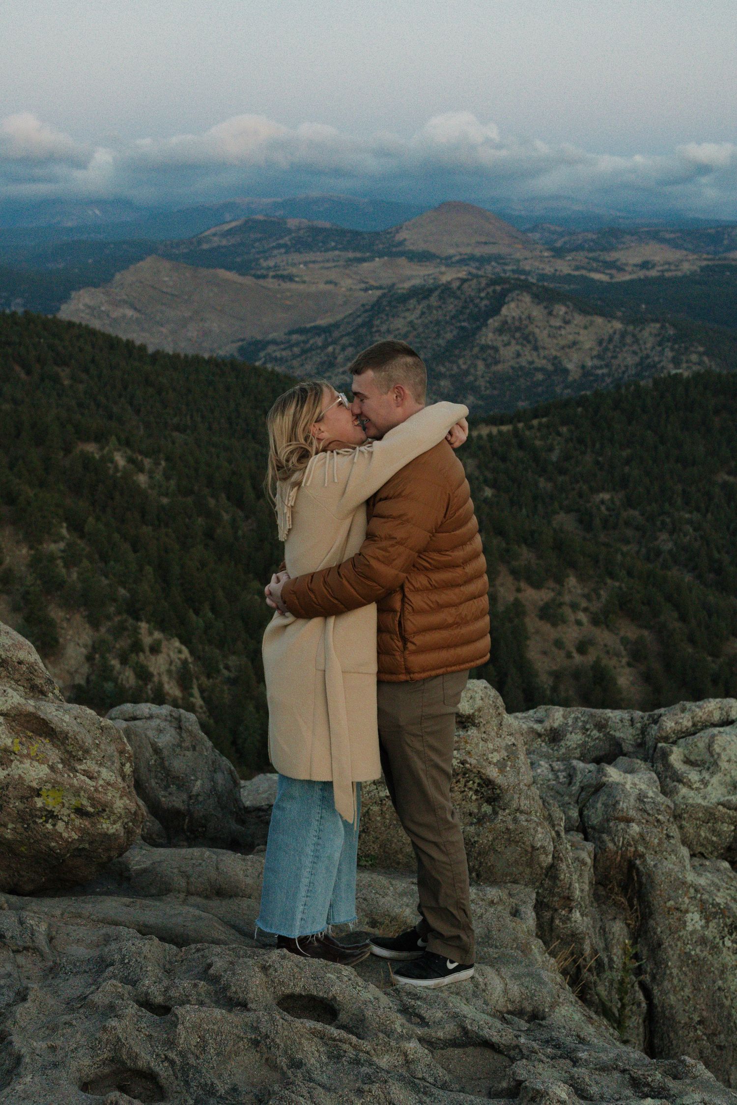 Couple embracing on a rocky mountain overlook surrounded by expansive mountain views during an intimate couples photography session
