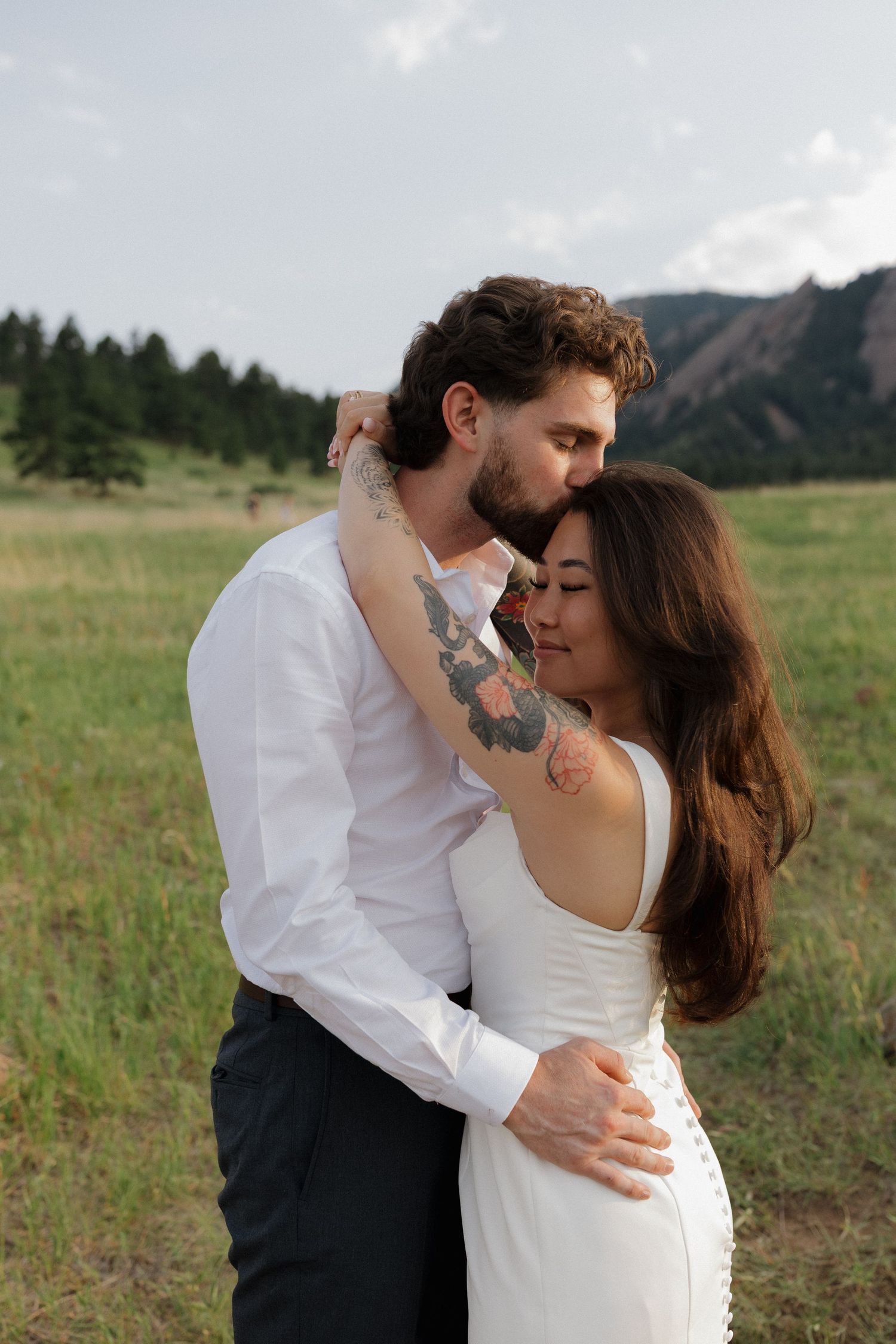 Couple embracing and sharing a kiss in an open meadow with mountain views during a romantic couples photography session