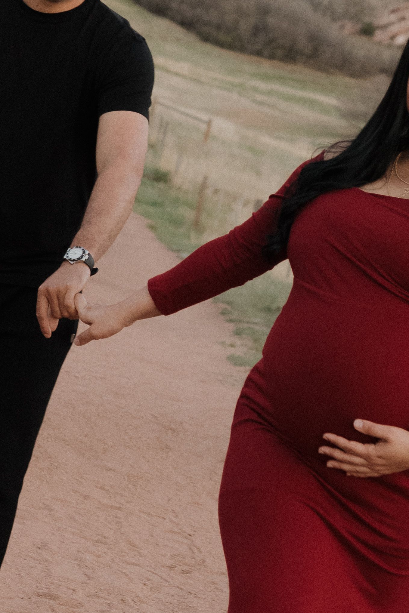 Pregnant woman in a flowing red maternity dress holding hands with her partner during an intimate outdoor maternity session