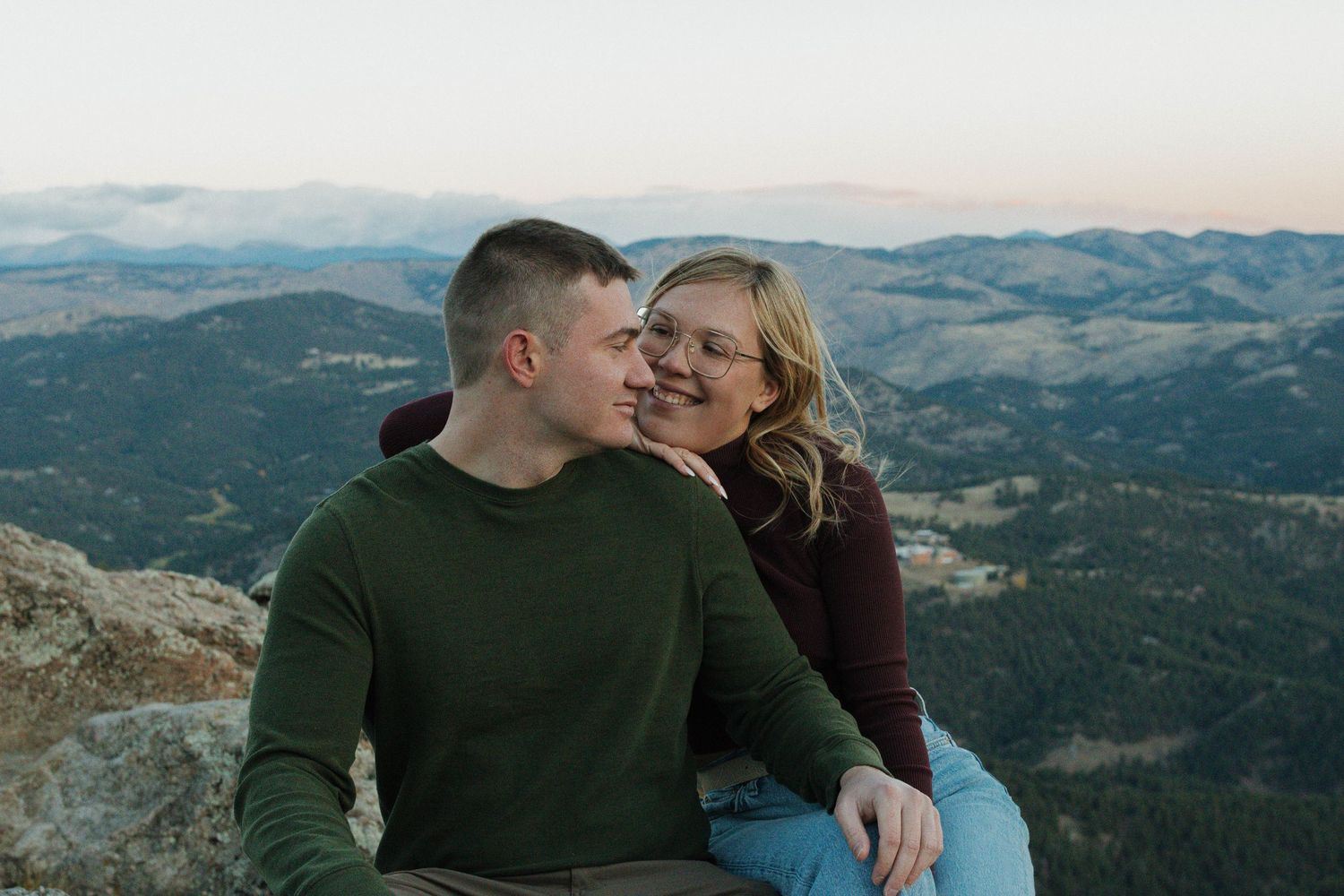 Couple sitting together and sharing a tender moment on a mountain overlook during a romantic couples photography session