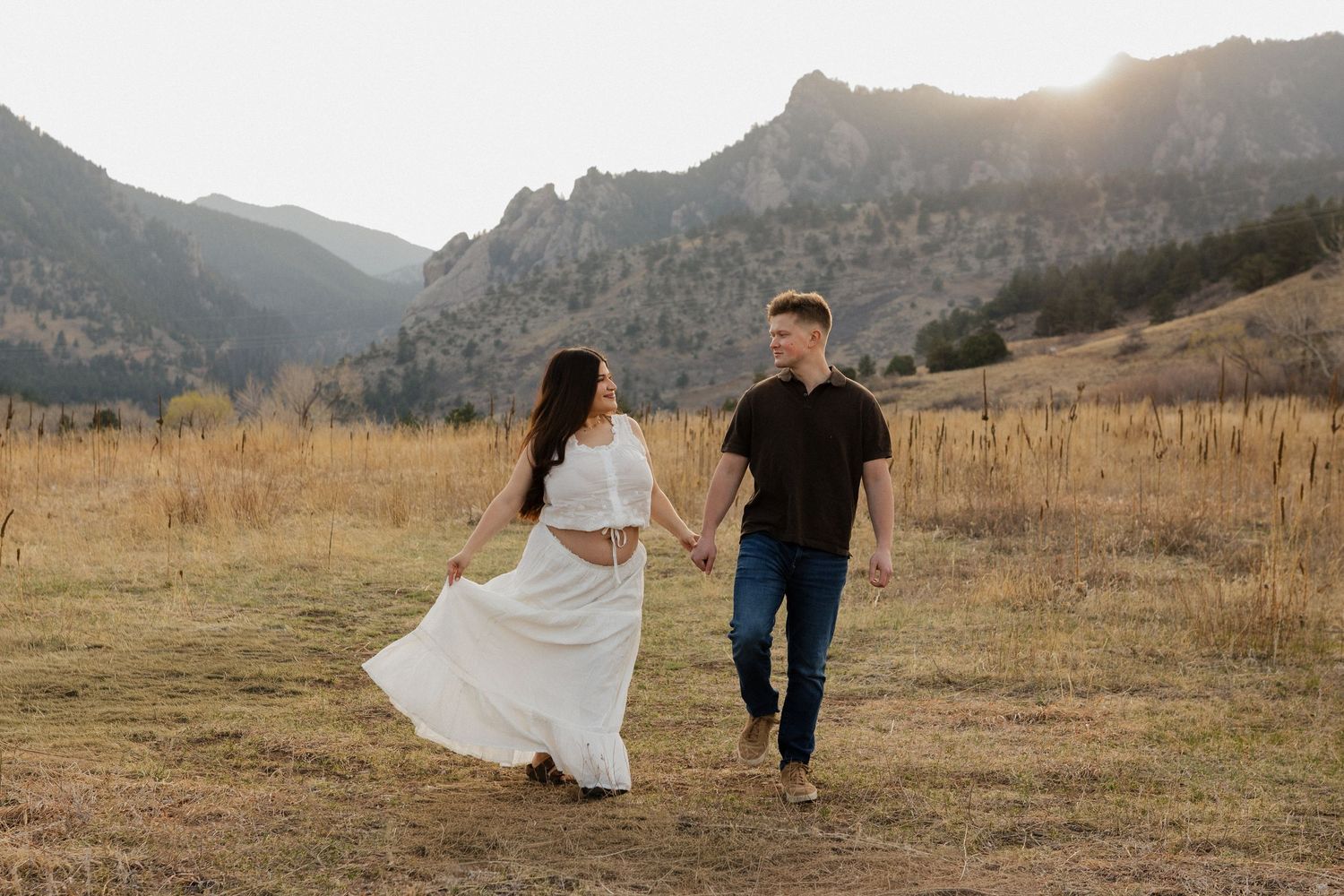 Expecting couple walking together through a Colorado mountain meadow during a natural maternity photography session