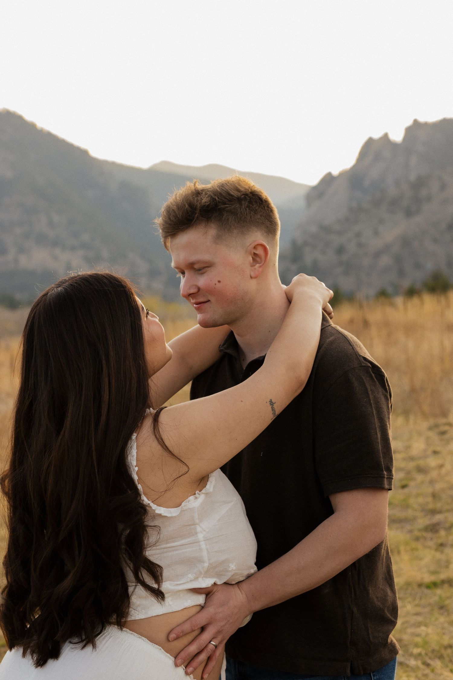 Expecting couple sharing an intimate moment outdoors during a romantic maternity photography session surrounded mountains