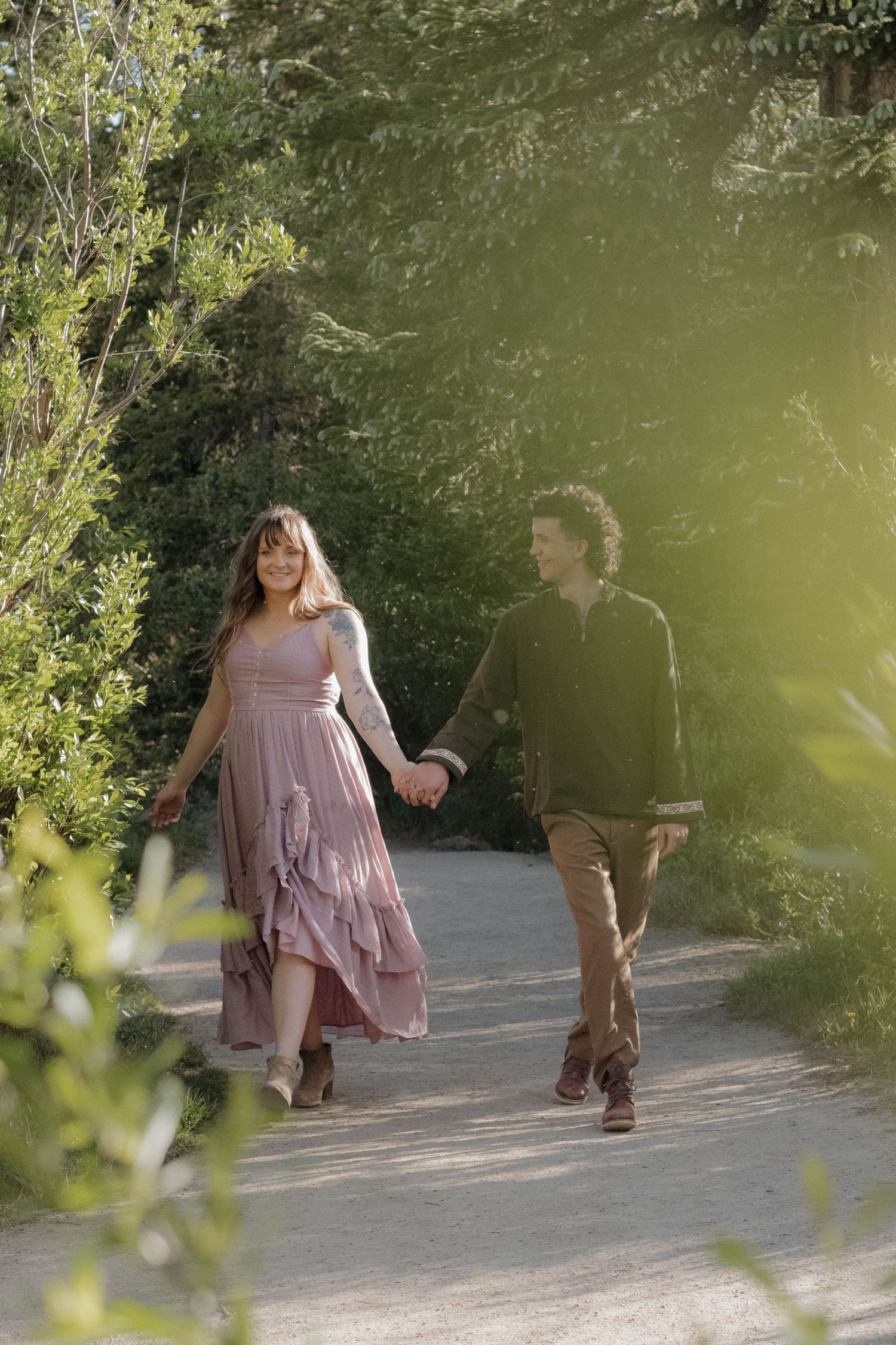 Couple walking hand in hand through a lush forest surrounded by soft natural light during a couples photography session