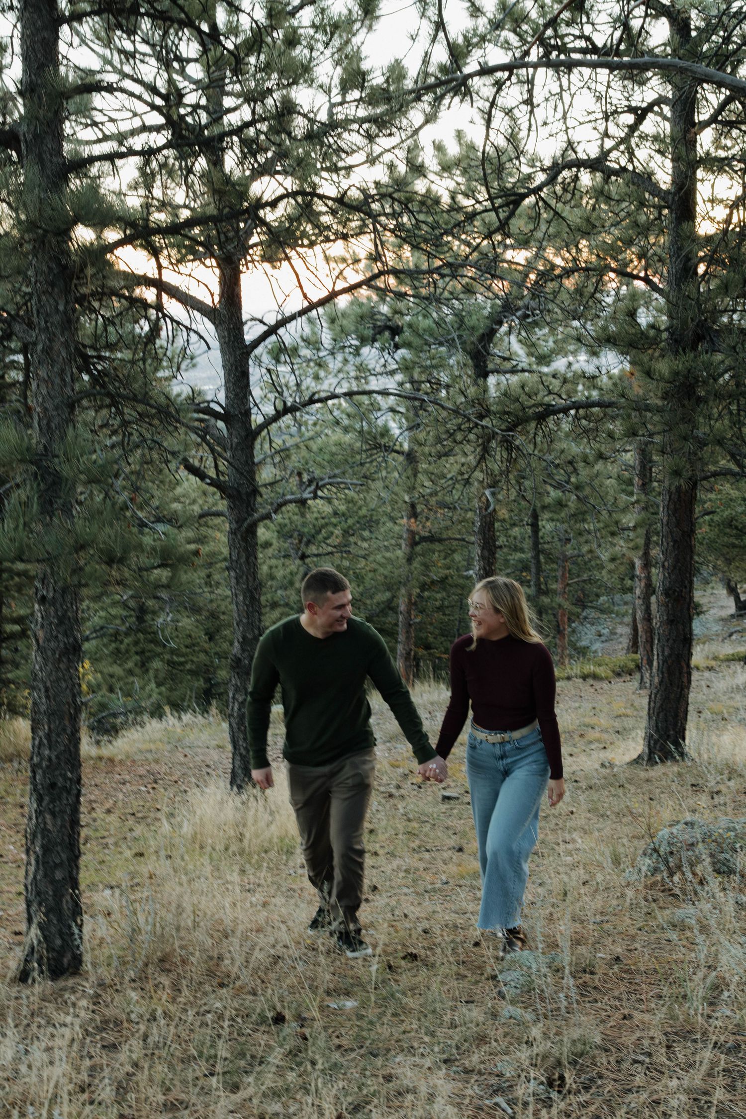 Couple walking hand in hand through a peaceful pine forest during a natural and intimate couples photography session