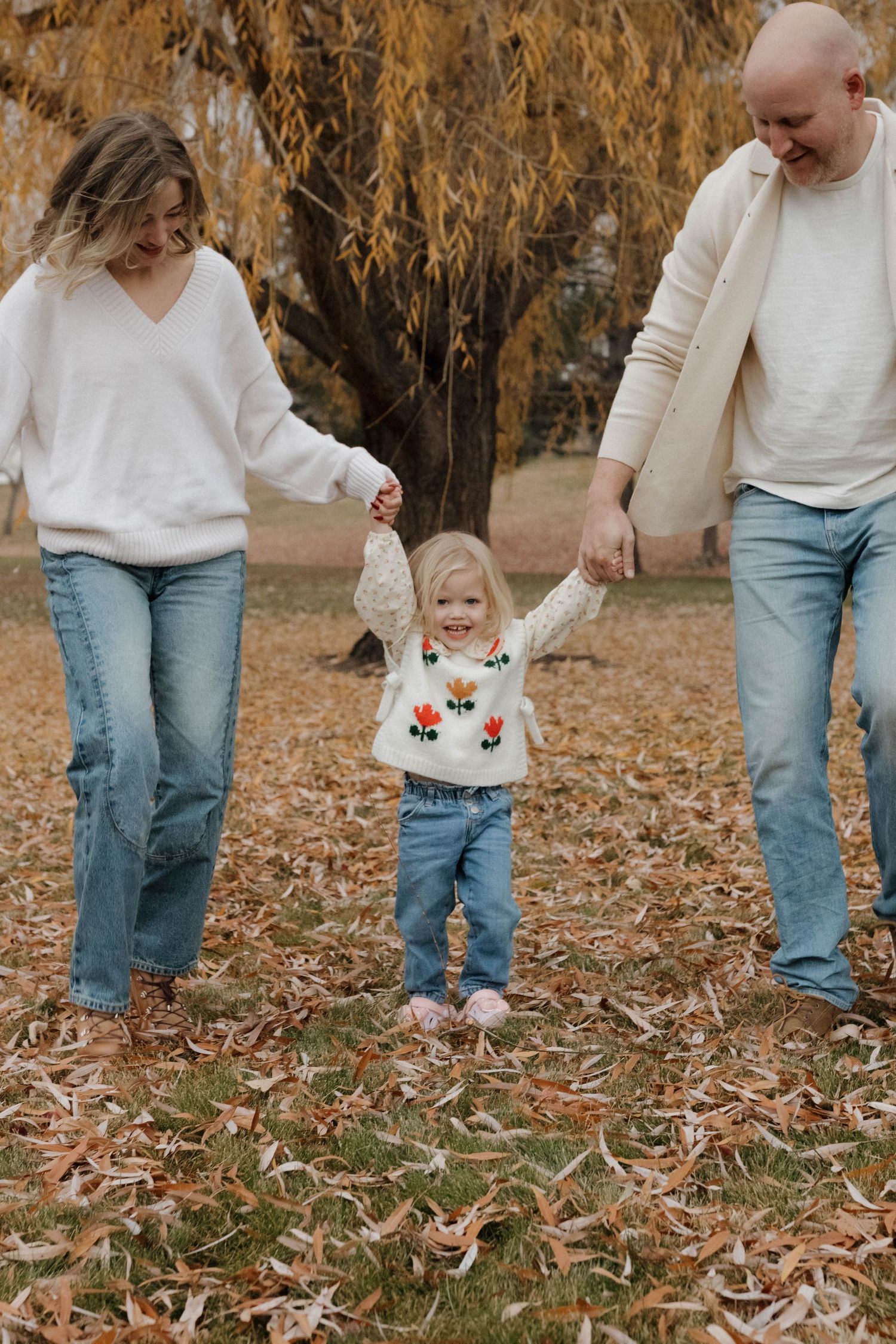 Parents walking hand in hand with their young daughter outdoors during a natural family photography session