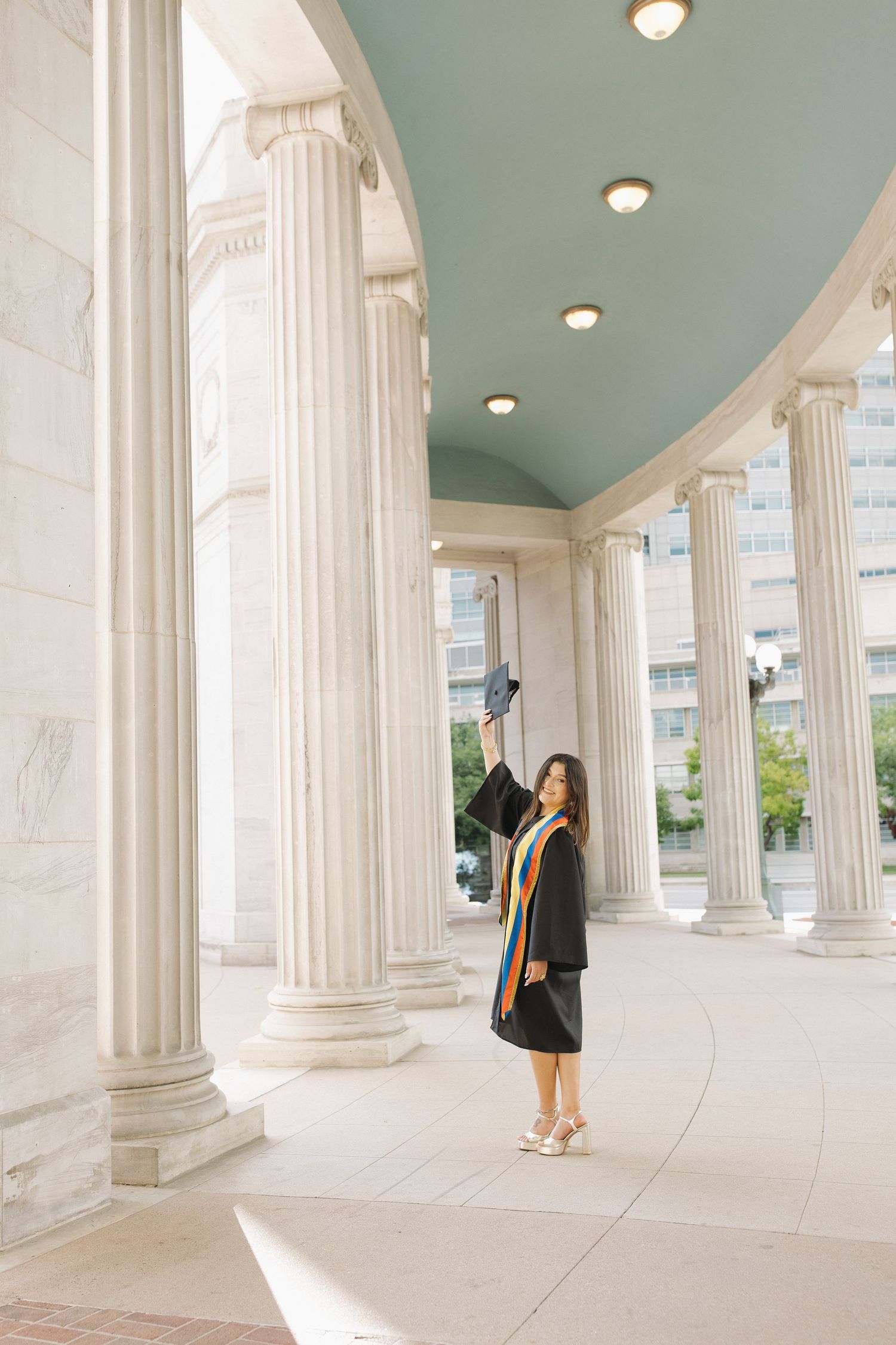 Young woman in graduation attire posing in a bright architectural setting during a graduation portrait session