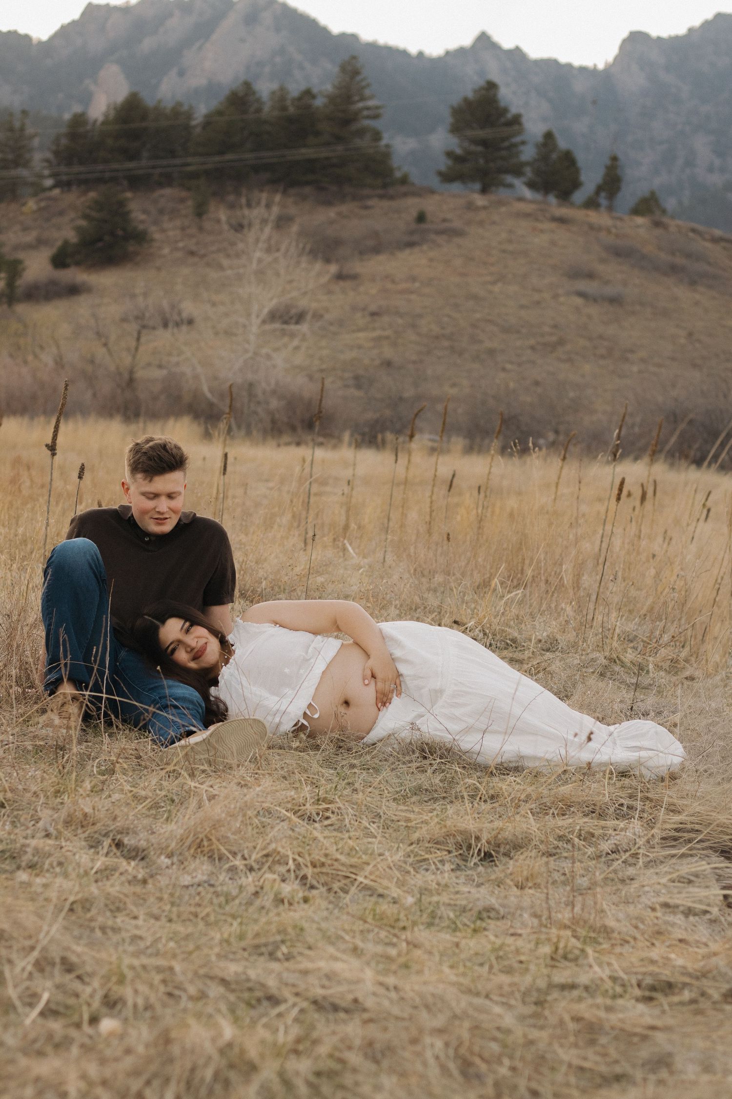 Expecting couple relaxing together in a mountain meadow during an intimate outdoor maternity photography session