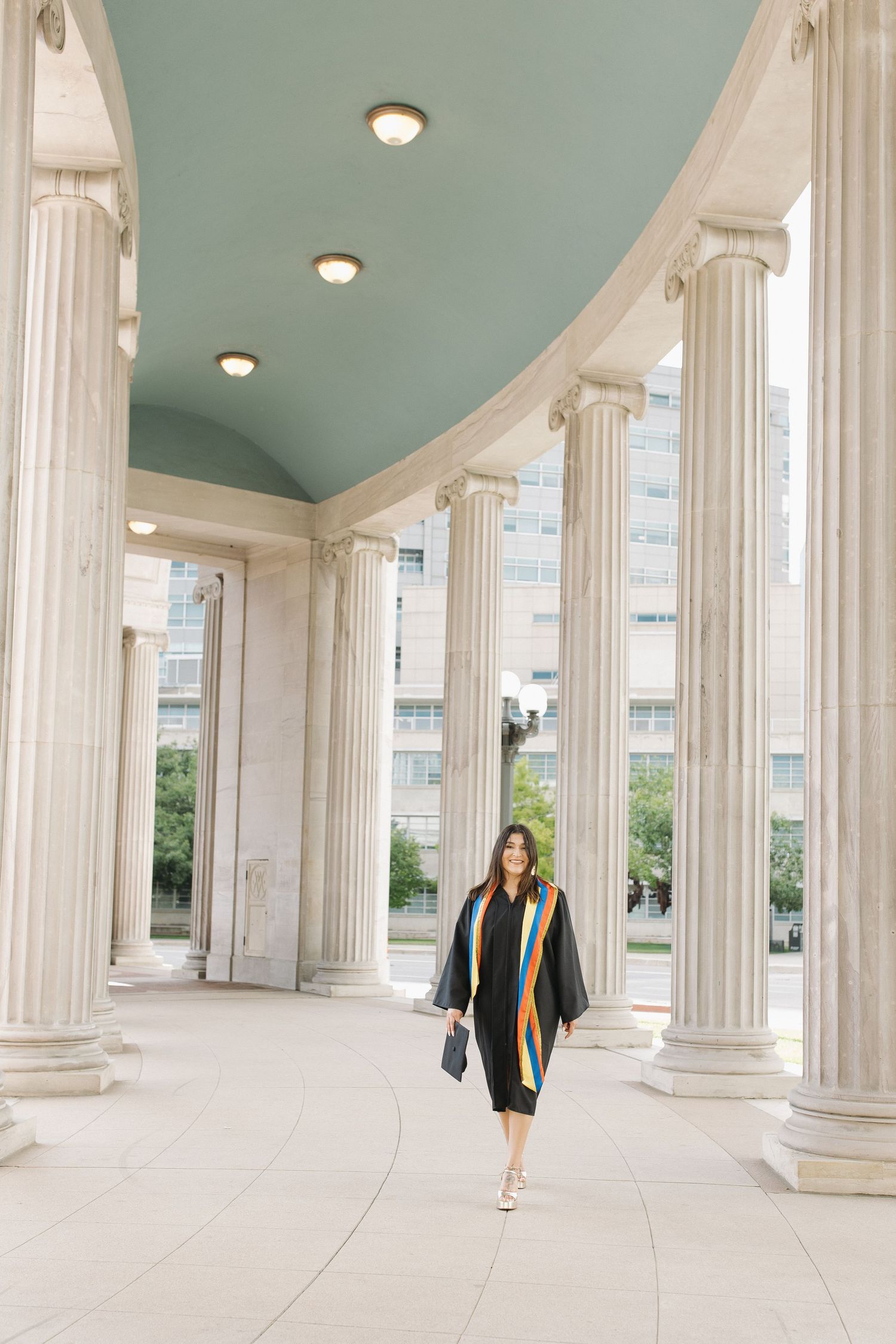 Young woman in a graduation cap and gown posing in an elegant interior during a graduation portrait session