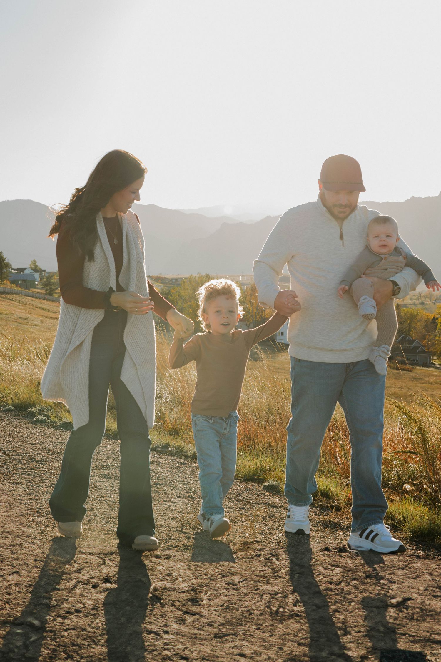 Family of four walking together outdoors in a sunlit meadow during a warm and natural family photography session