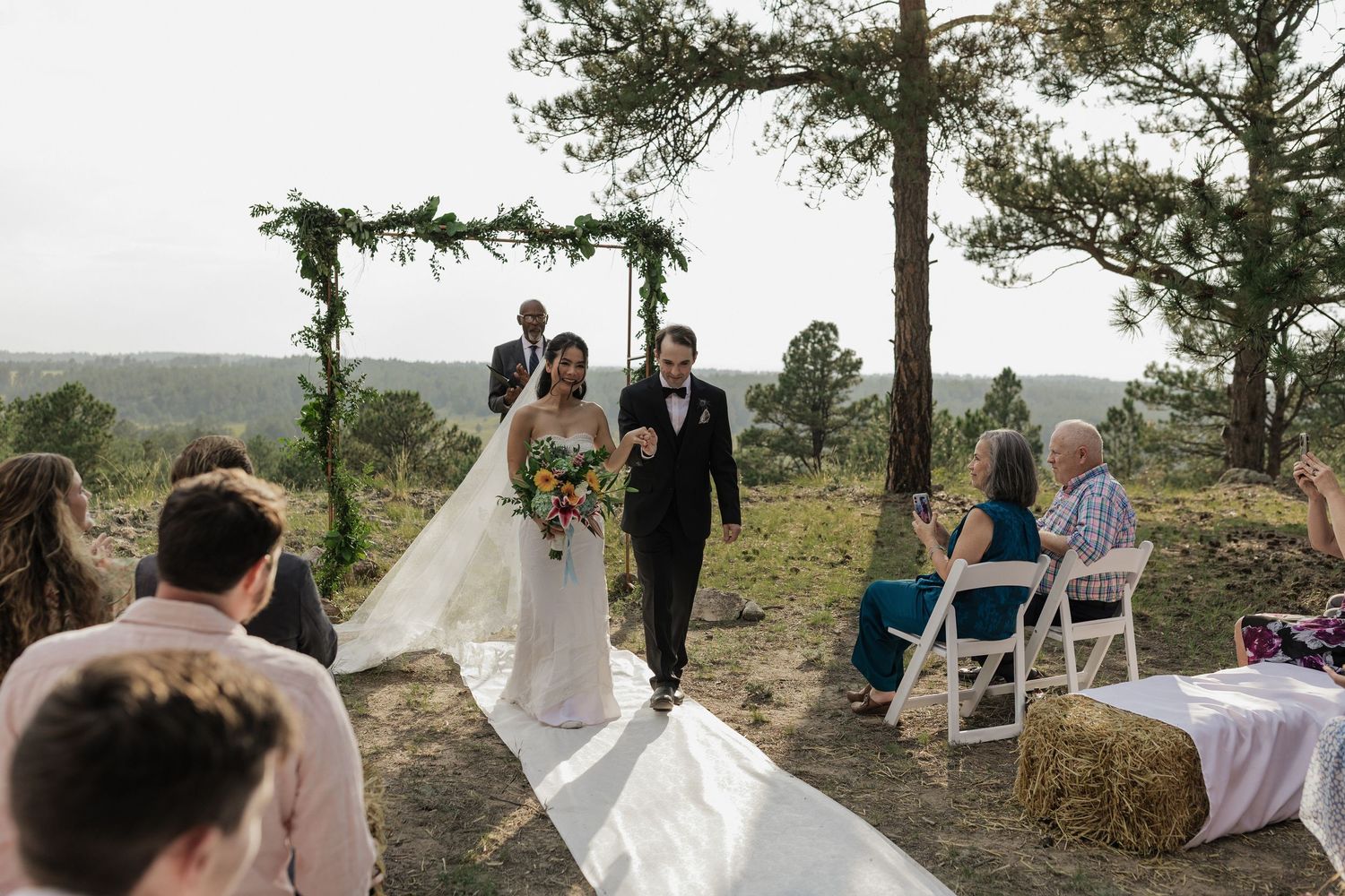 Bride and groom walking hand in hand through the trees after their wedding ceremony