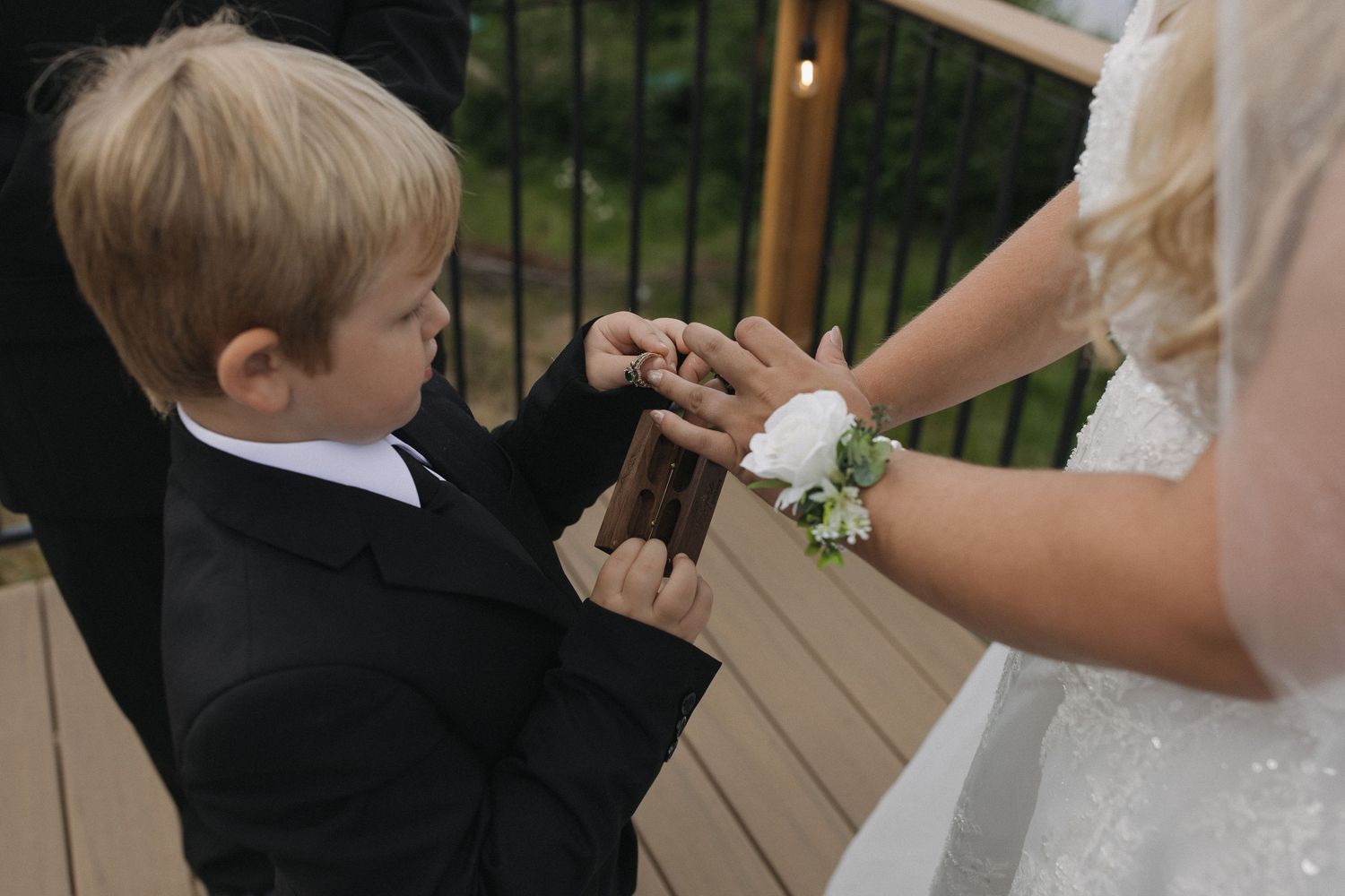 Young boy holding the bride’s hand during a wedding ceremony on a lakeside deck