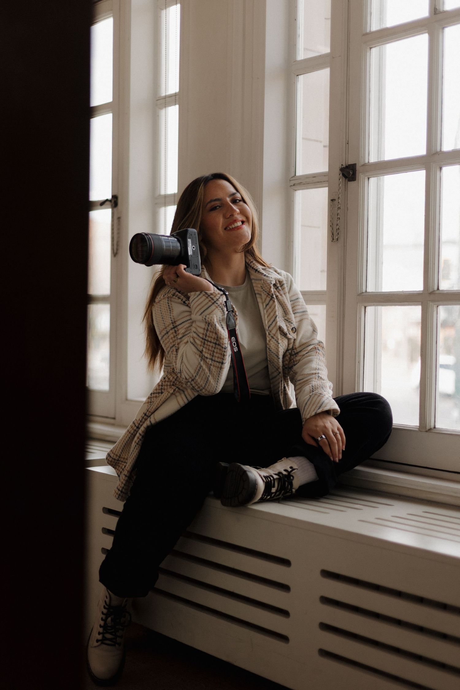 Natalia, photographer behind Love & Light, holding a camera while sitting by a window
