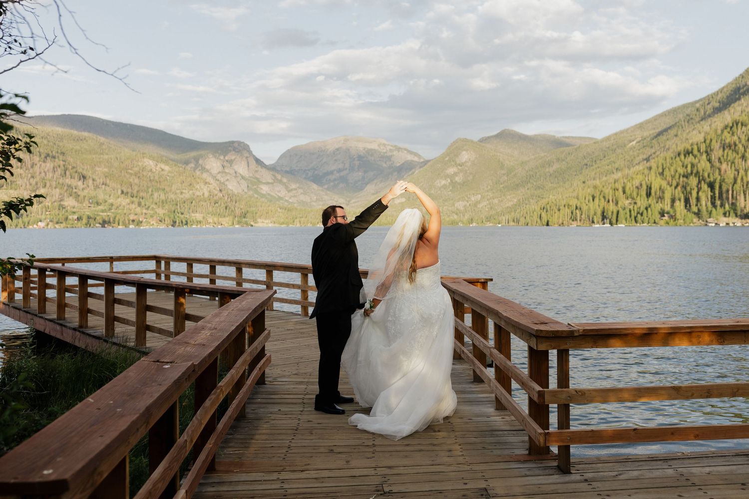 Bride and groom embracing on a wooden deck overlooking a mountain lake