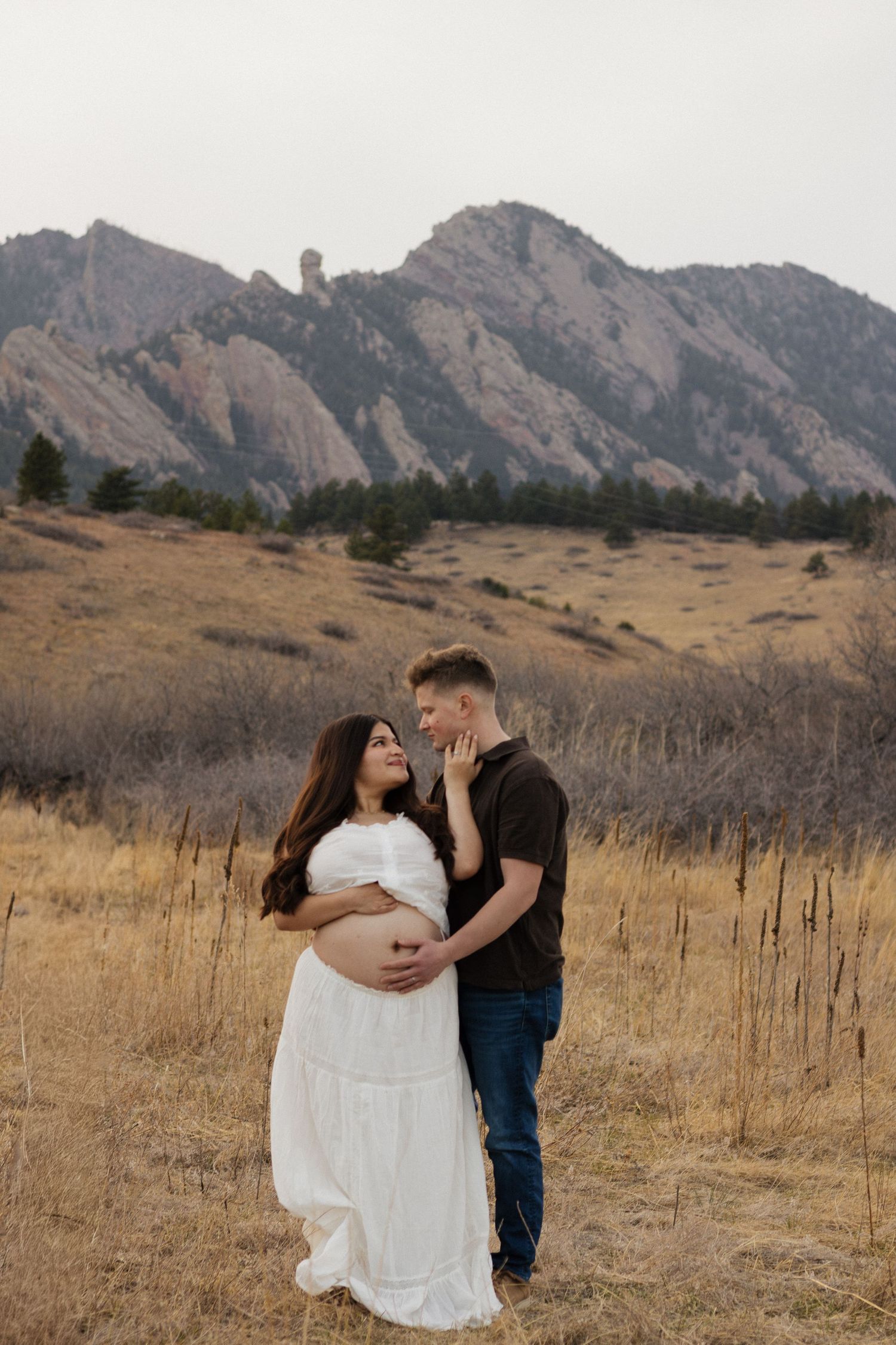 Expecting couple embracing in a mountain meadow during an intimate outdoor maternity photography session