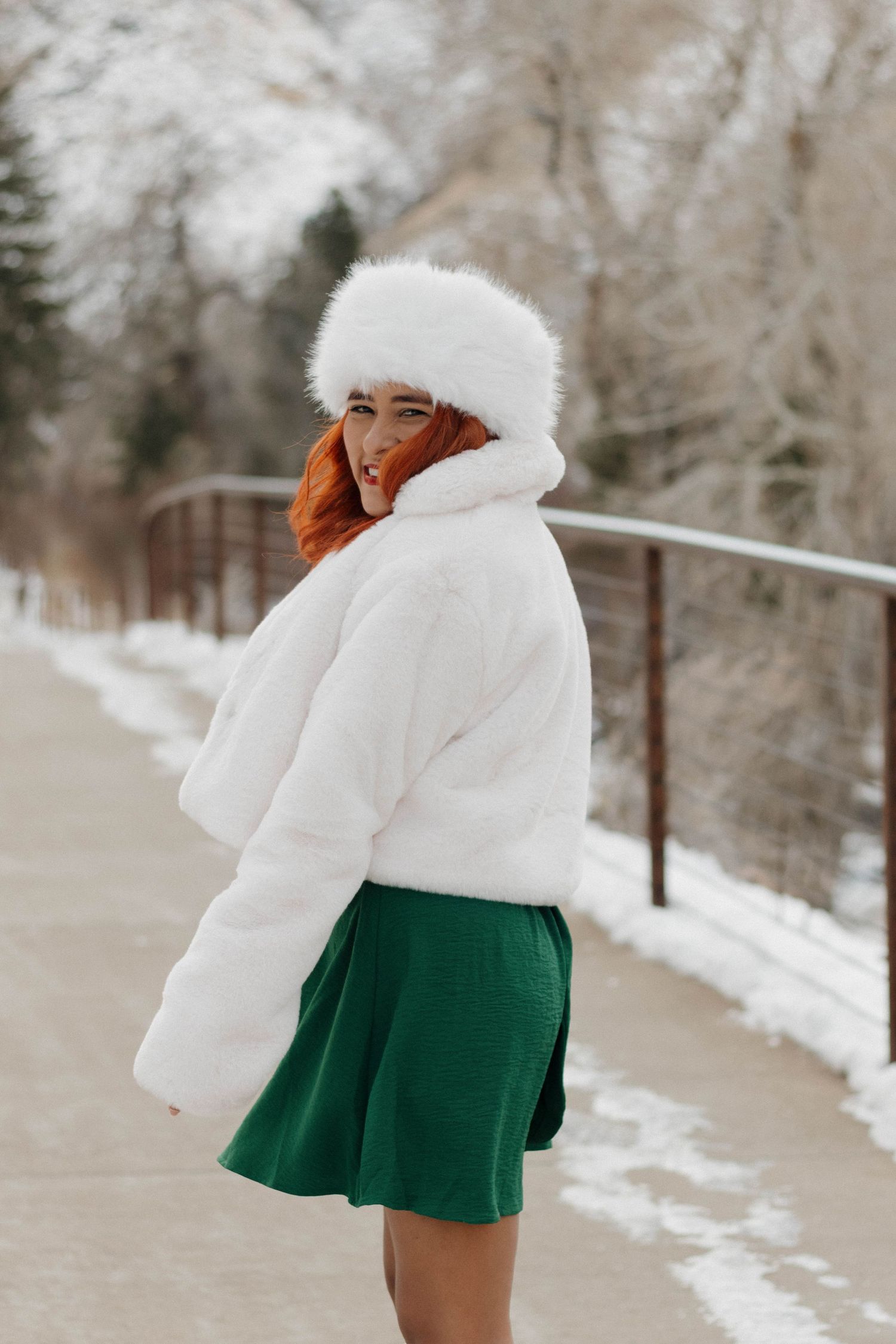 Woman in a white winter hat and green skirt posing outdoors in a snowy landscape during a portrait session