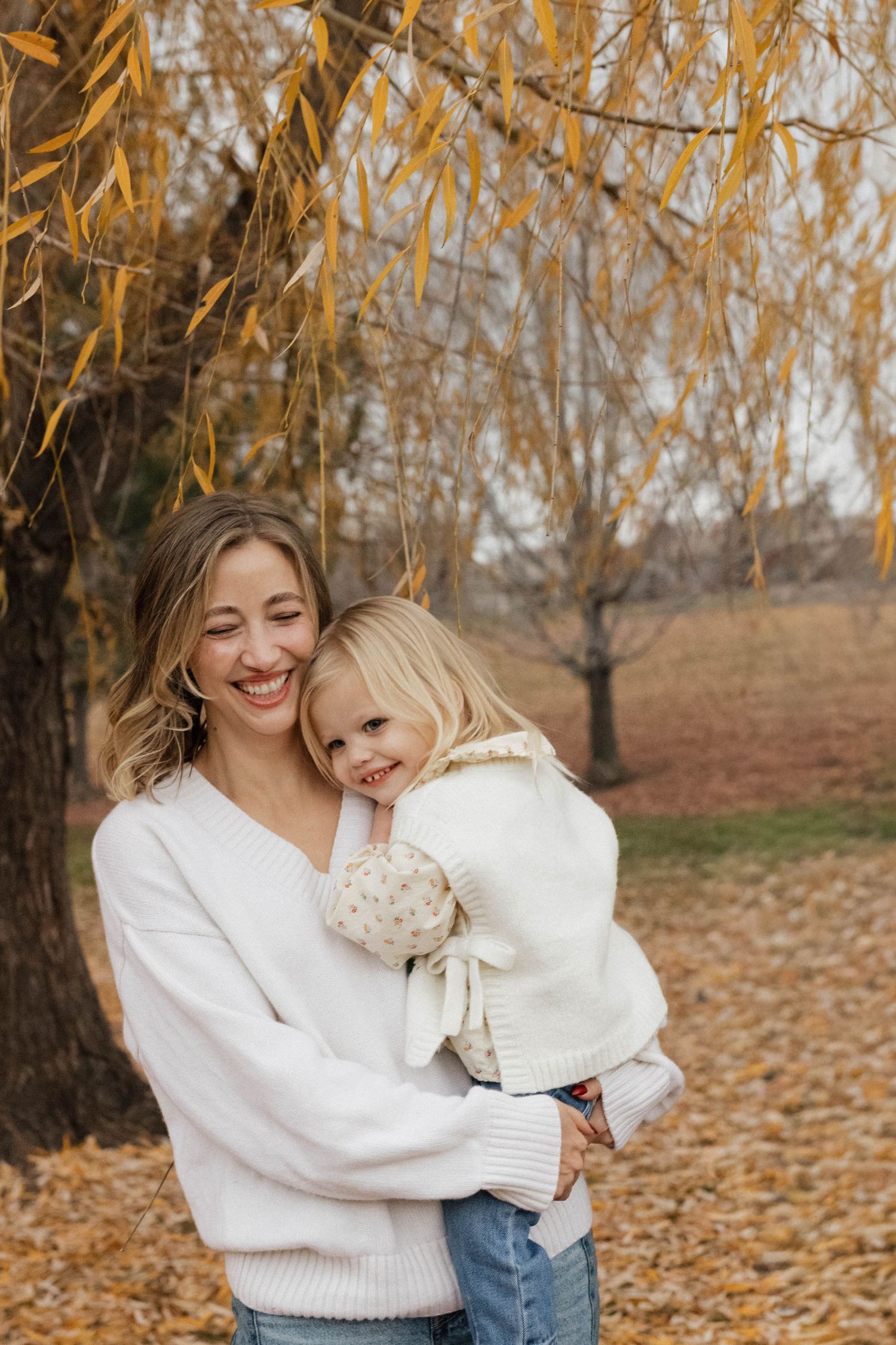 Mother holding her young daughter outdoors surrounded by golden autumn foliage during a natural family photography session