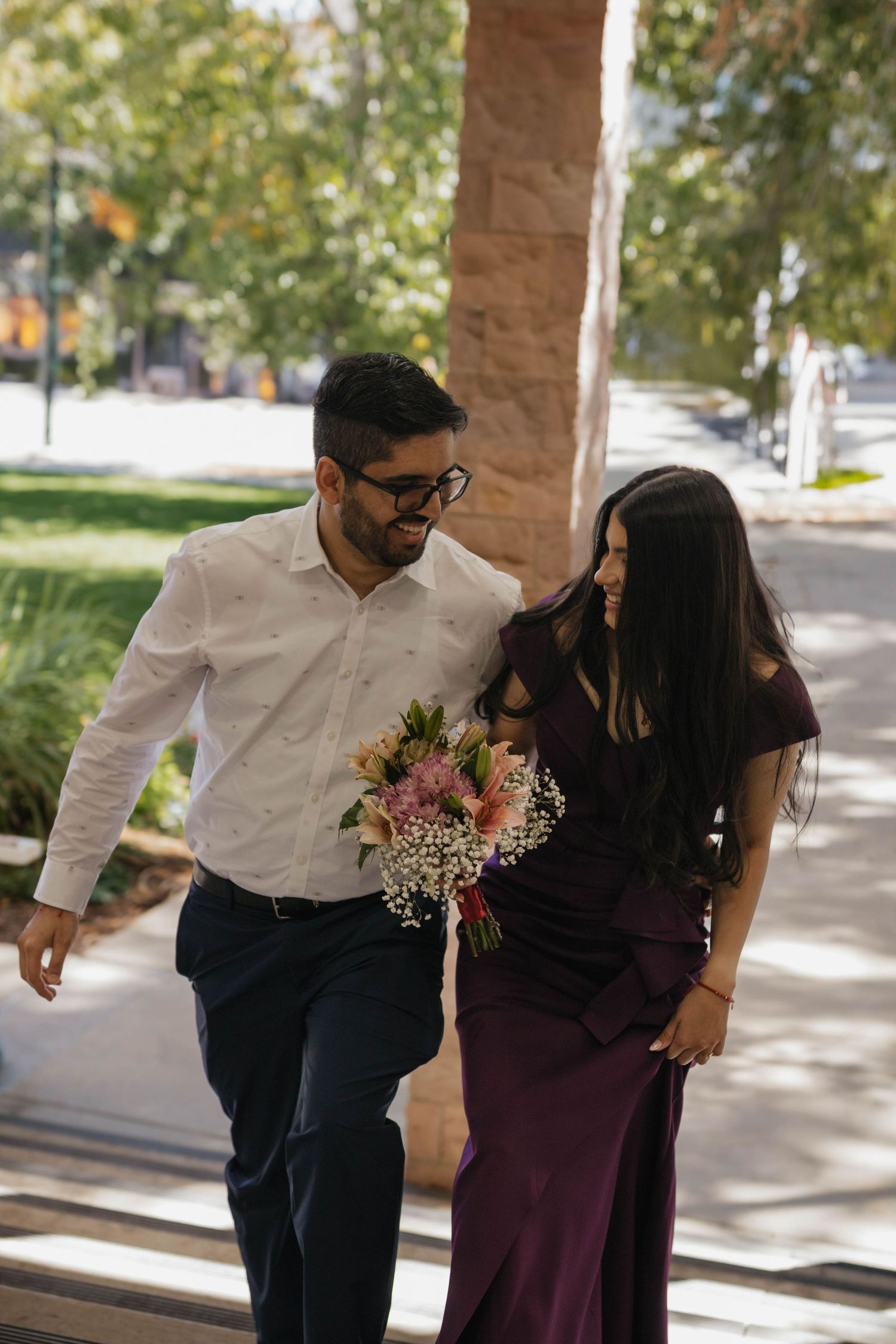 Engaged couple walking together outdoors while carrying a bouquet during their engagement session