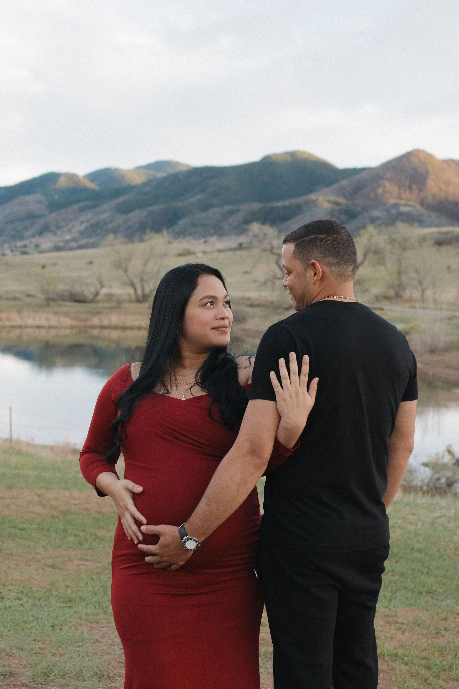 Pregnant woman in a red maternity dress sharing a moment with her partner against a Colorado mountain landscape