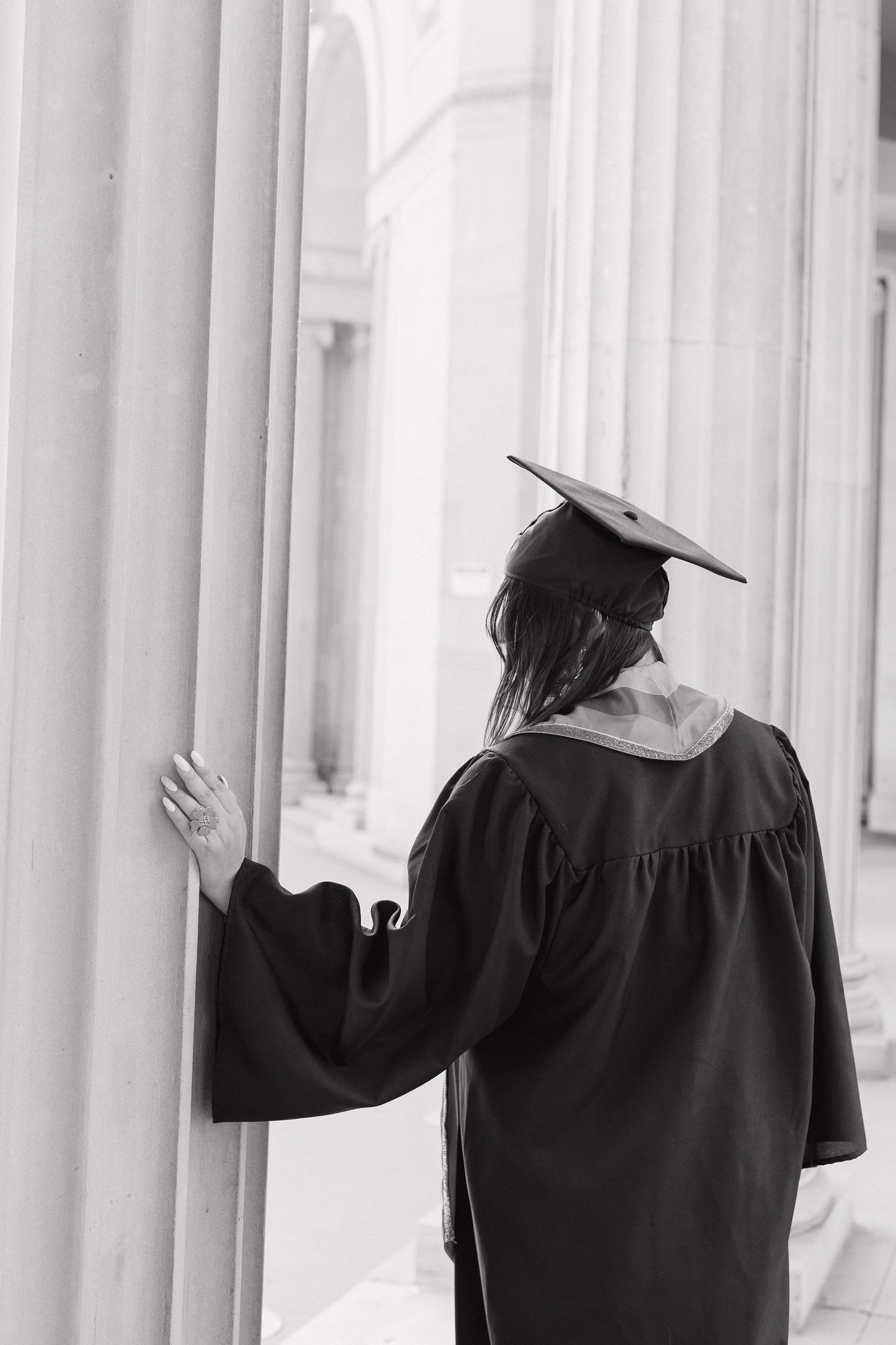 Black and white graduation portrait of a young woman in a cap and gown, captured in an elegant editorial style