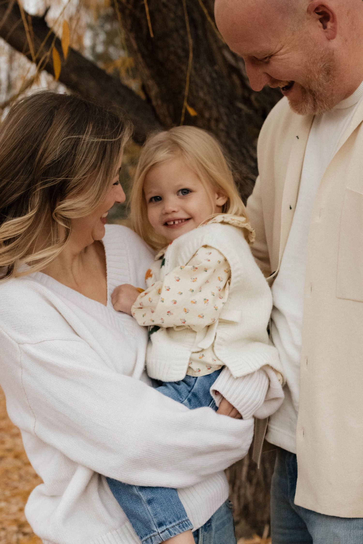 Parents cuddling their young daughter outdoors among the autumn trees during a warm and natural family photography session