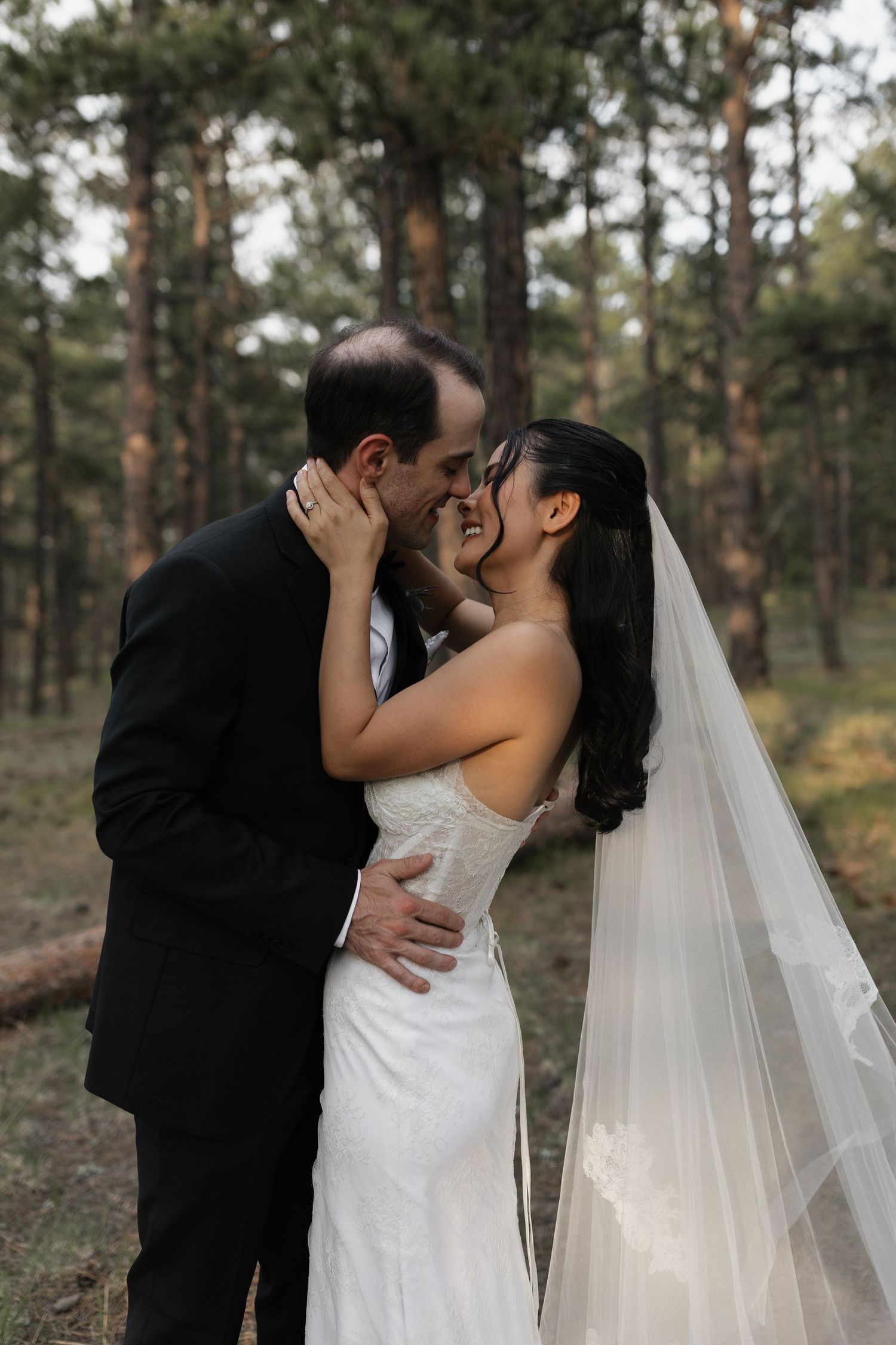Bride and groom embracing and sharing a kiss outdoors among the trees