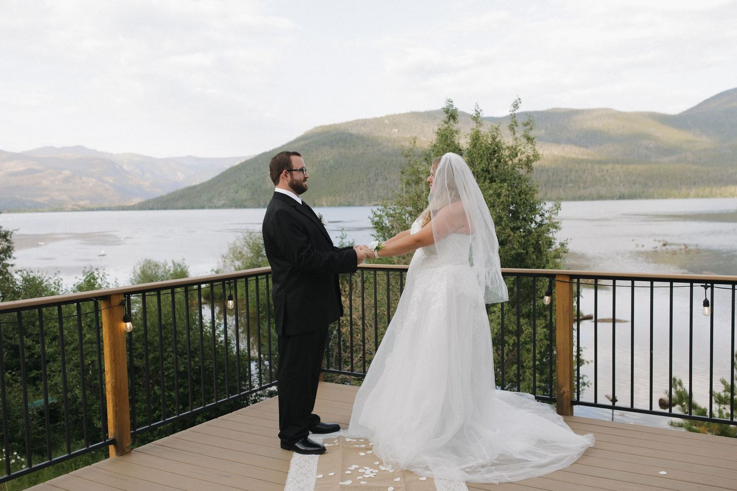 Bride and groom standing together on a lakeside deck with mountains in the background