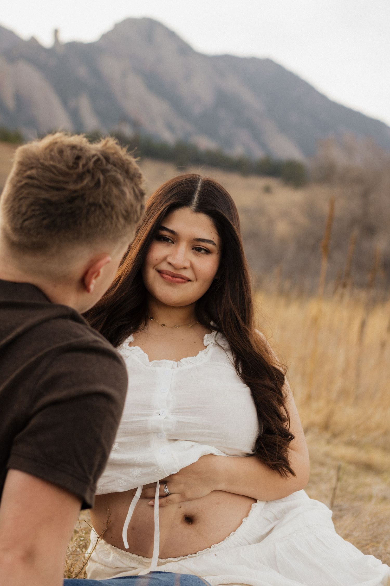 Pregnant woman smiling at her partner during a romantic outdoor maternity photography session in the mountains