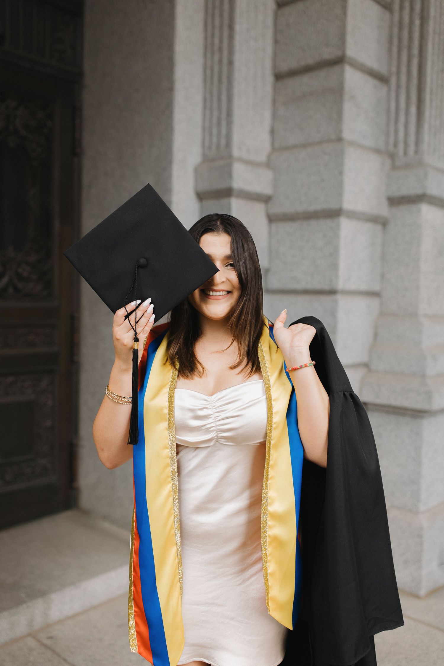 Graduate in cap and gown walking through a bright architectural space during an elegant portrait session