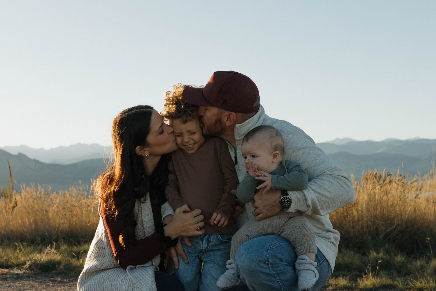 Parents cuddling with their two children outdoors in a Colorado mountain meadow during a natural family photography session