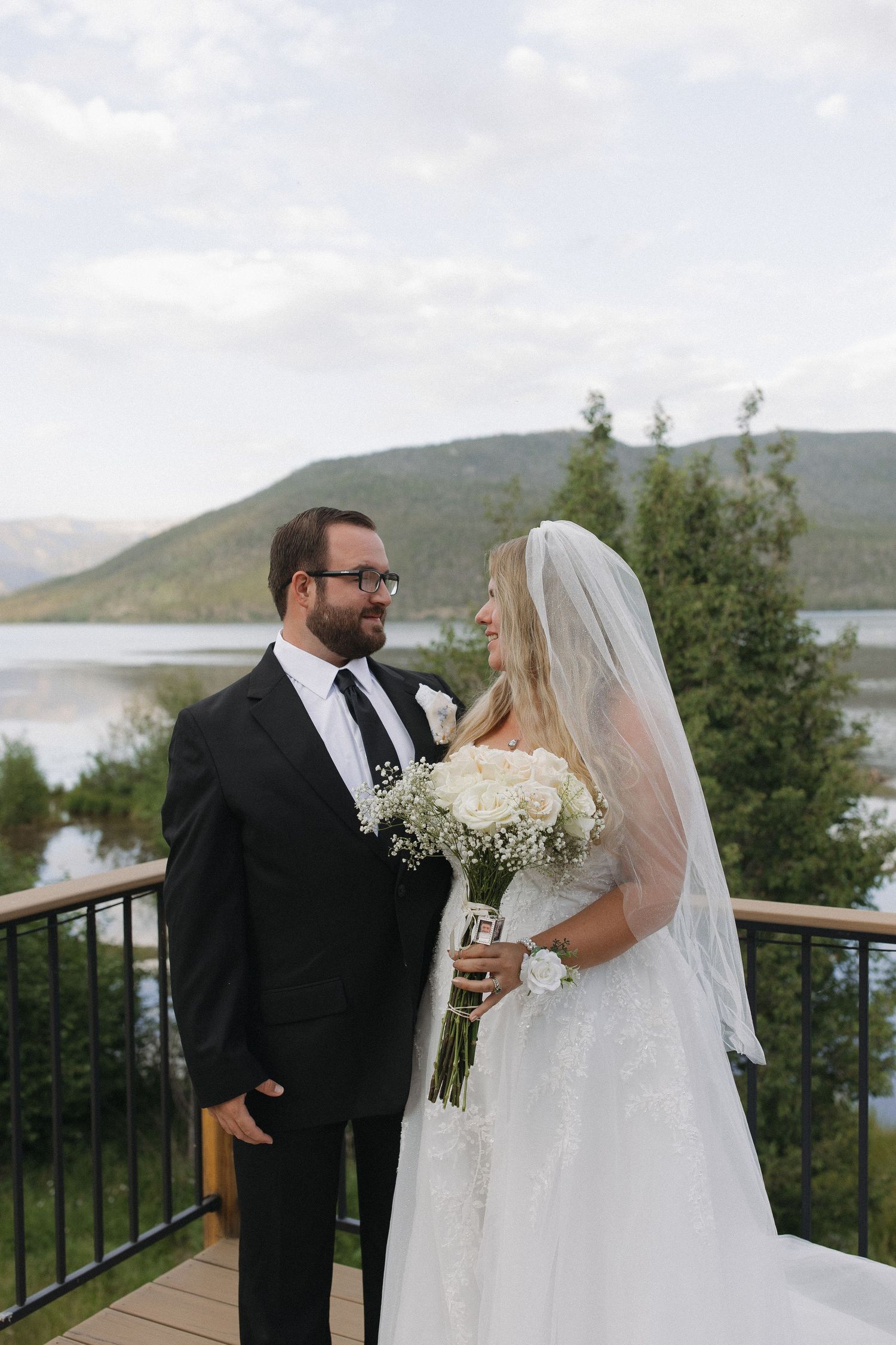 Bride and groom standing together on a lakeside deck with mountains in the background