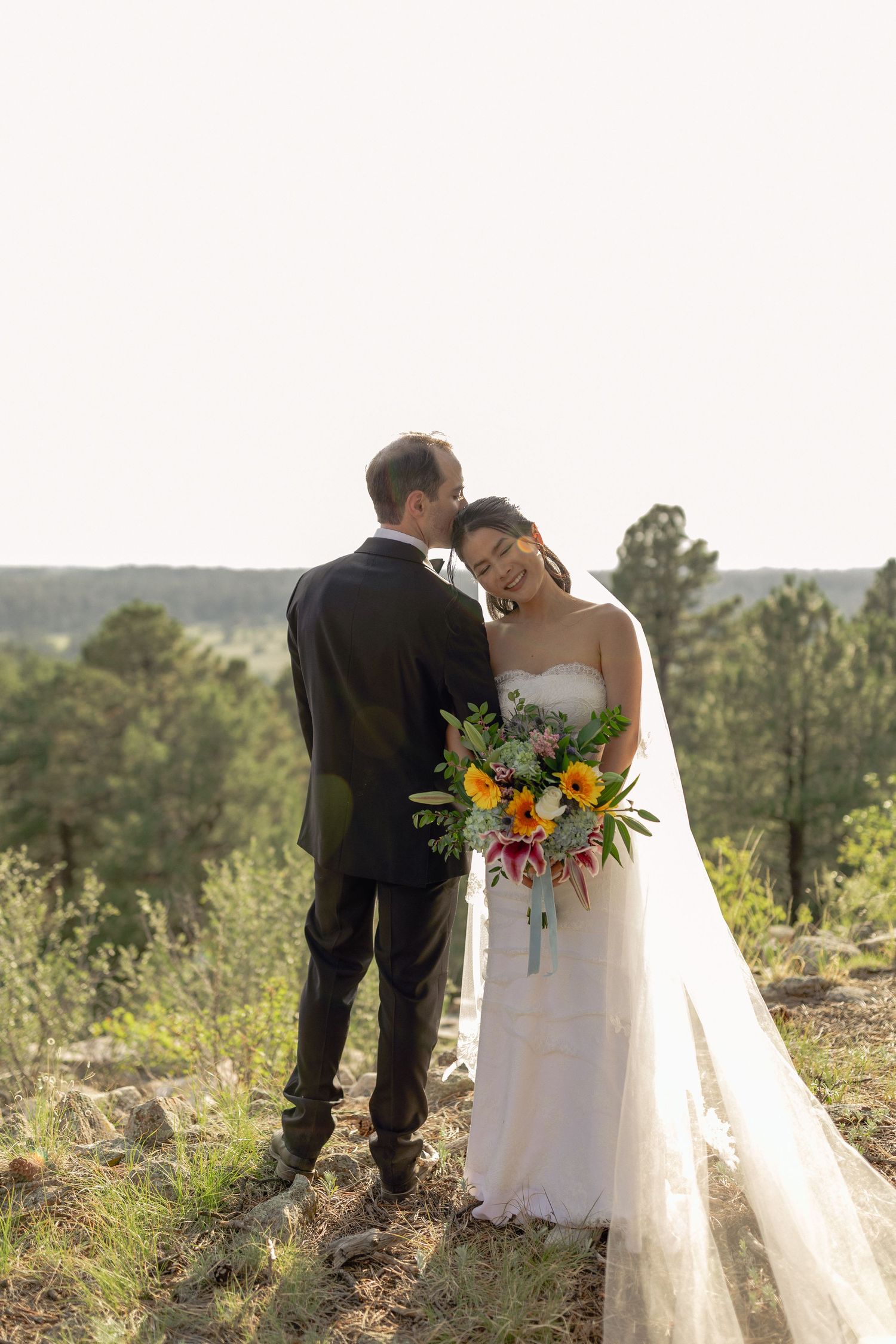 Bride and groom embracing outdoors with mountains and trees in the background