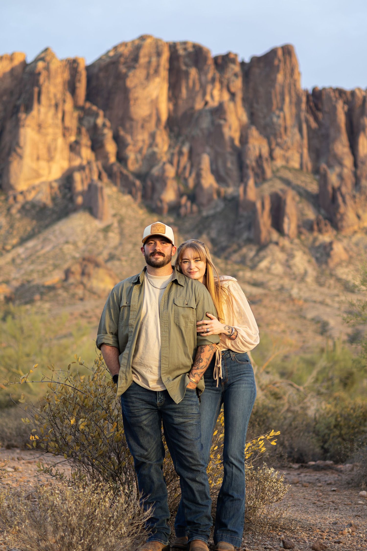 Couple embracing in desert landscape with Superstition Mountains at golden hour in Arizona.