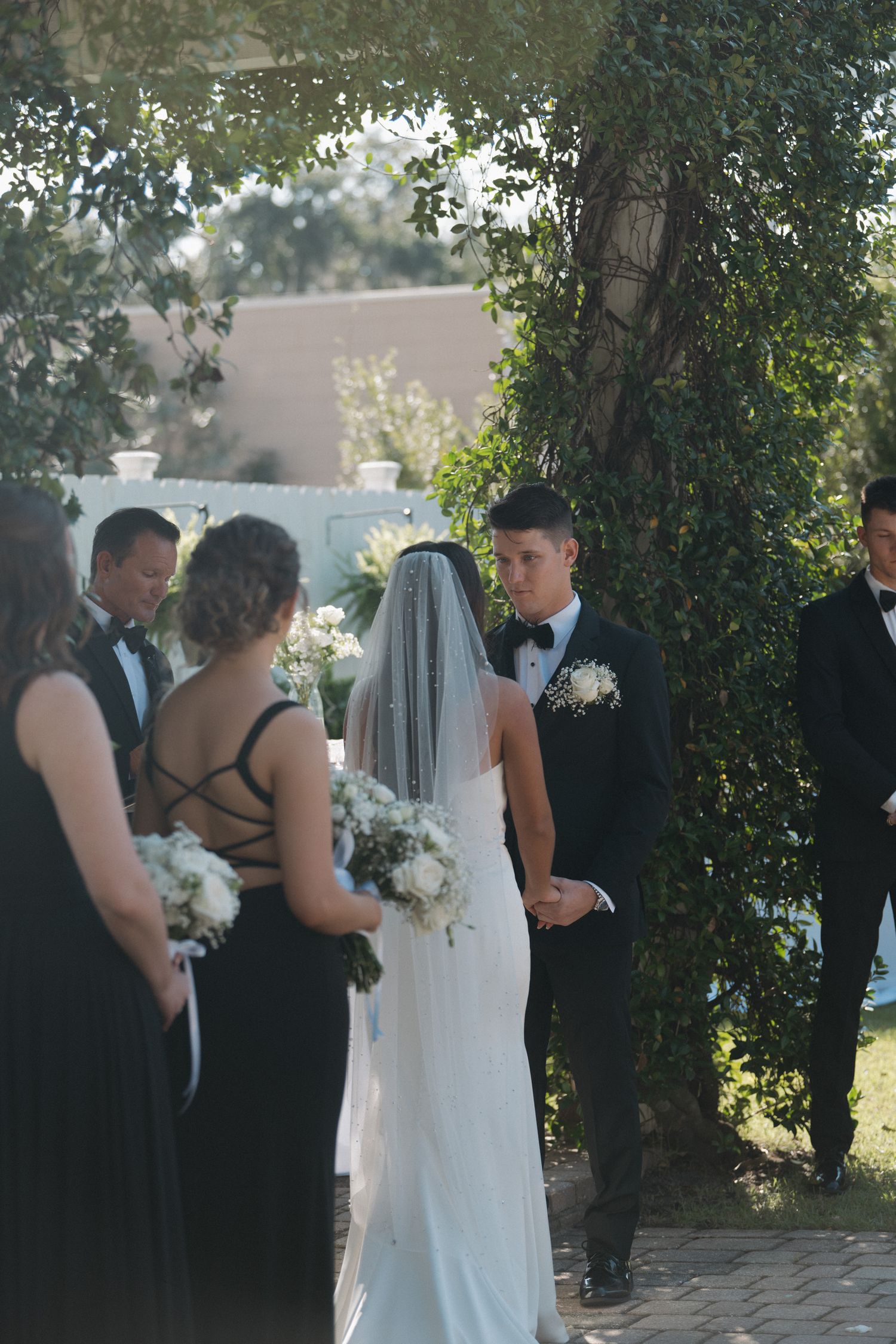 Bride and groom exchange vows at an outdoor wedding ceremony surrounded by bridesmaids and groomsmen.