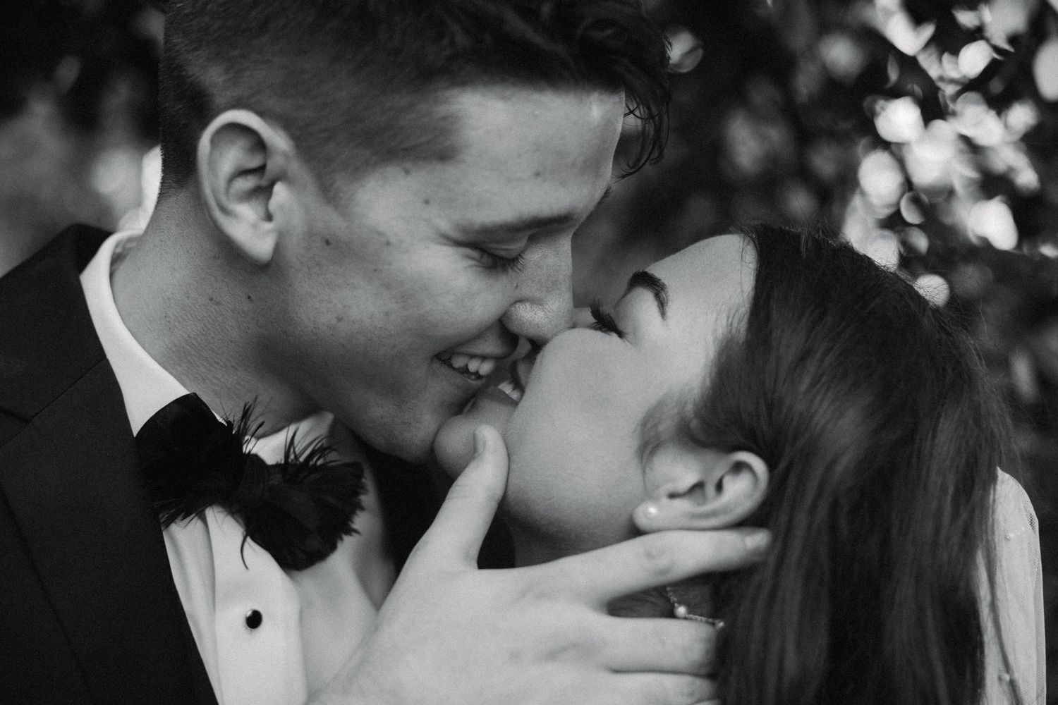 Black and white photo of smiling bride and groom sharing a romantic kiss.