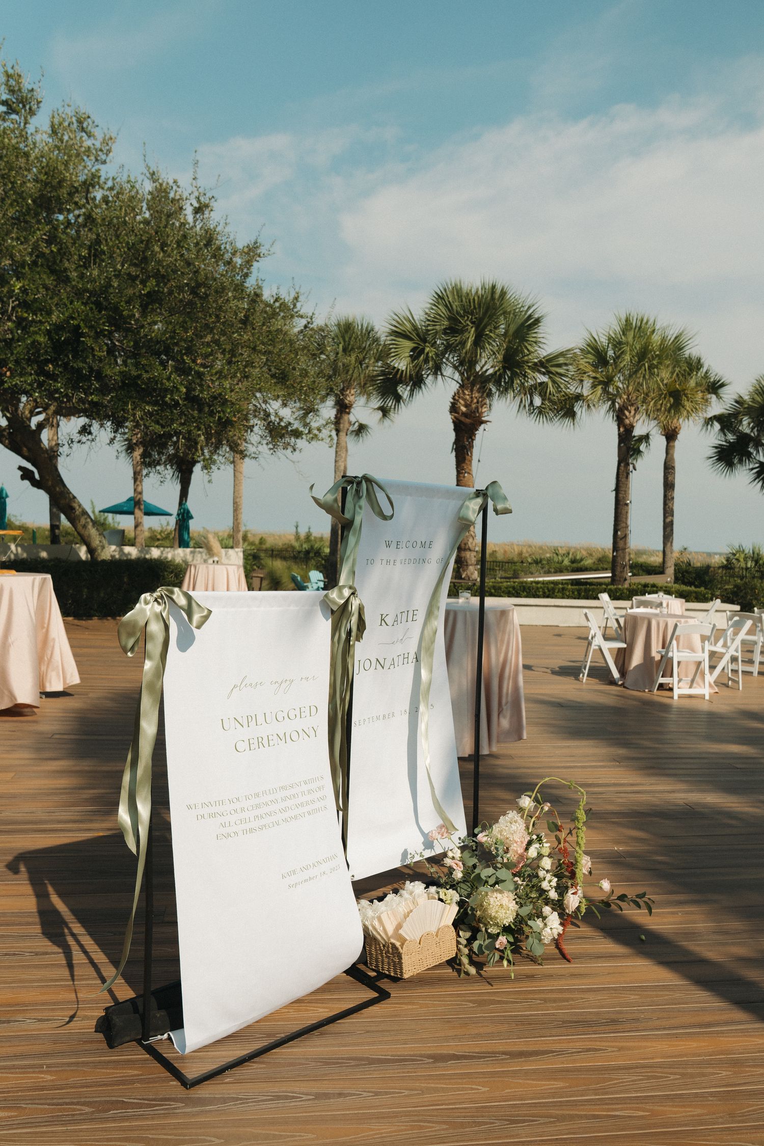 Outdoor wedding ceremony setup with elegant signage, floral arrangements, and palm trees.