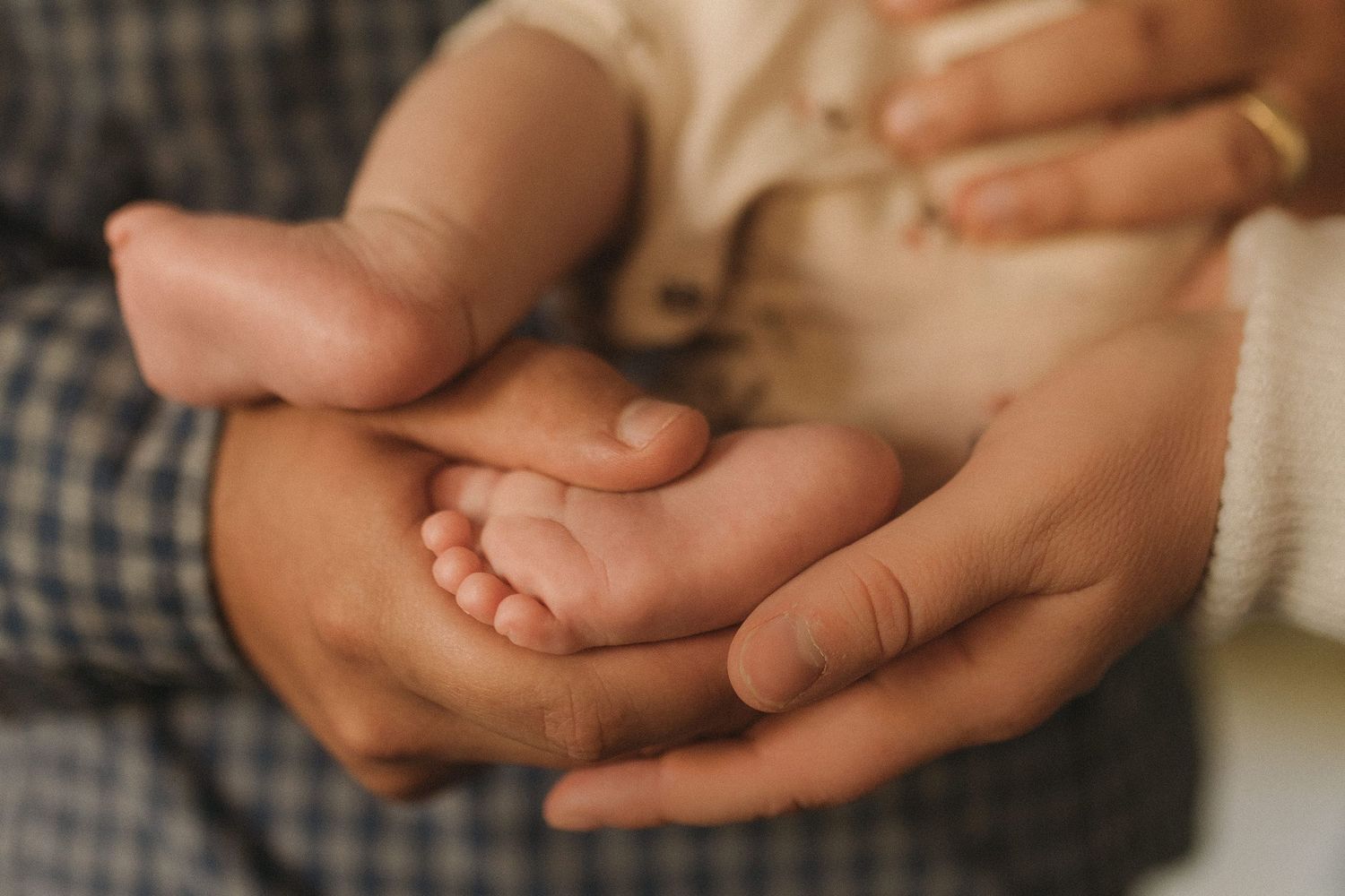 Close-up of parents hands cradling tiny newborn baby feet in soft light.