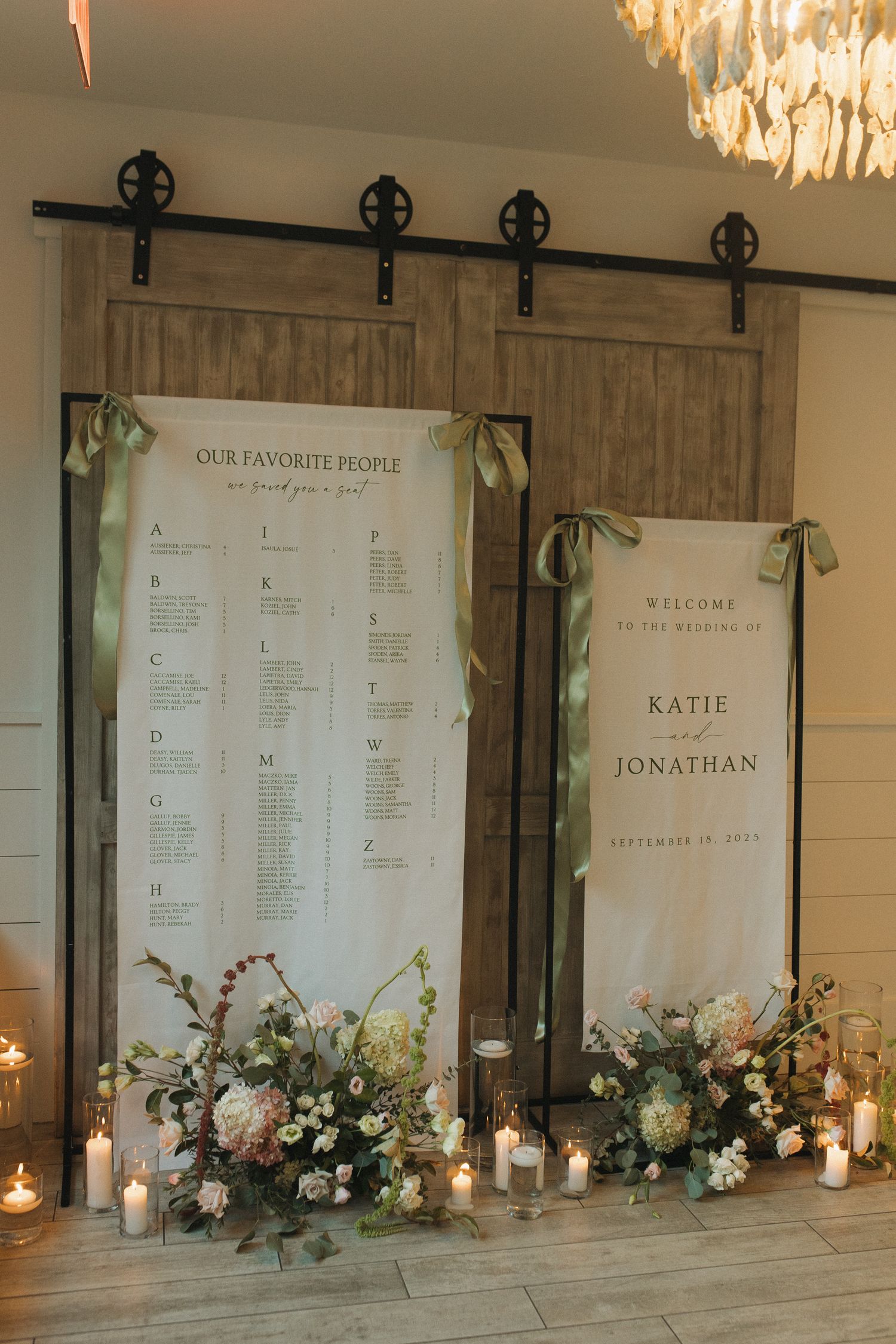 Elegant wedding seating chart display on rustic barn doors with floral arrangements and candles for Katie and Jonathan.