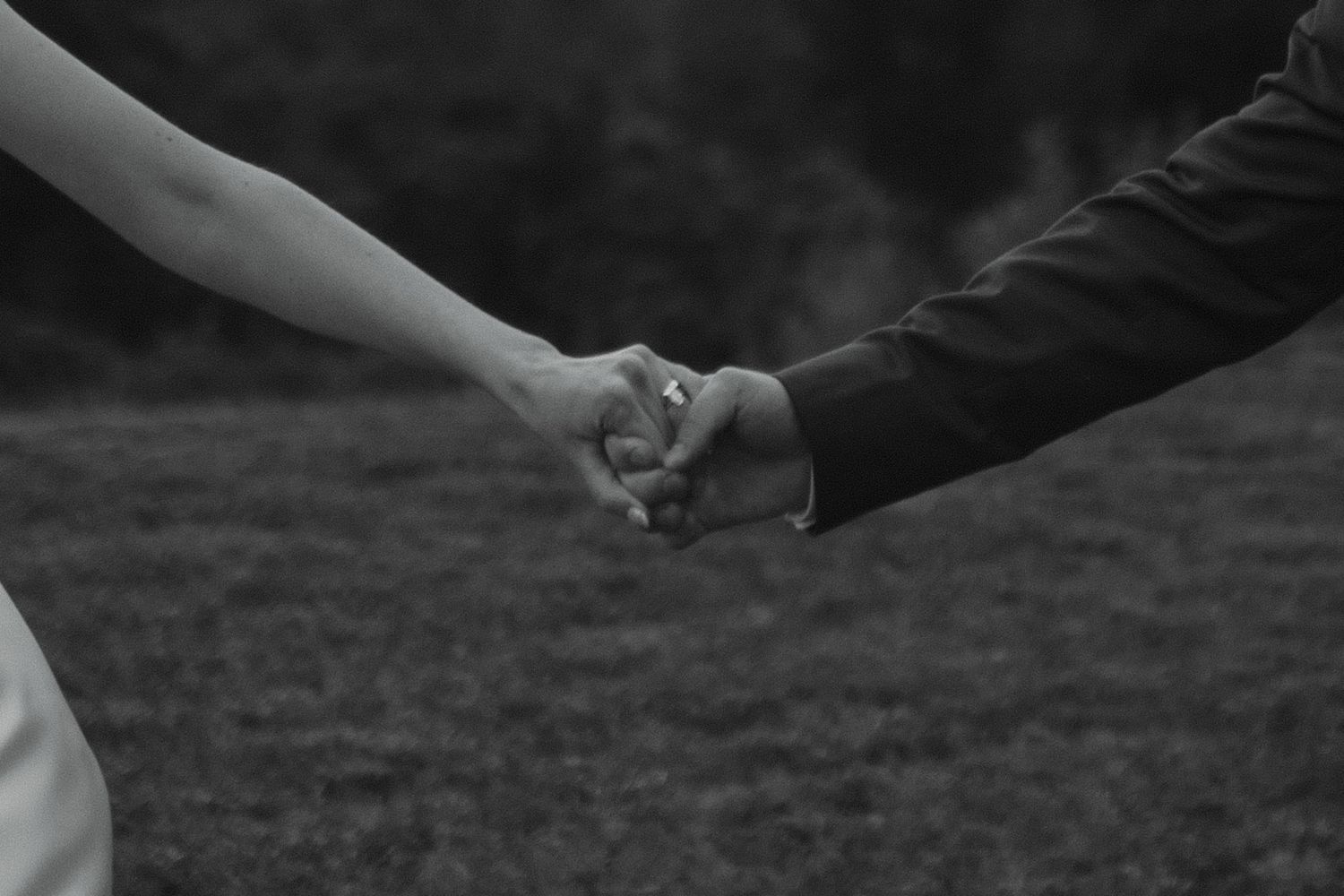 Black and white close-up of bride and groom holding hands on a green grass background.