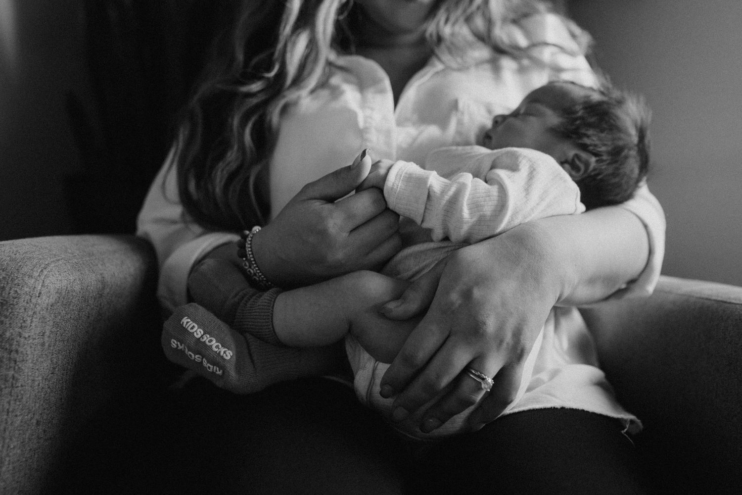 Black and white photo of a mother cradling her newborn baby while seated in a chair.