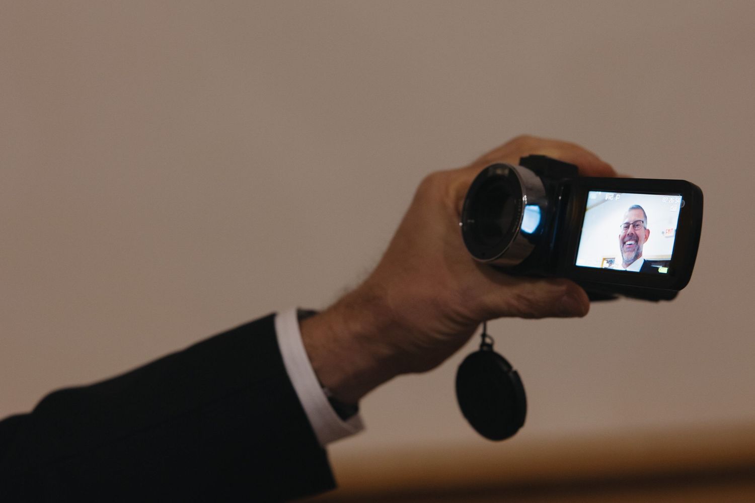 A hand holding a small camera displaying a smiling man's face on its screen, with a keychain attached.