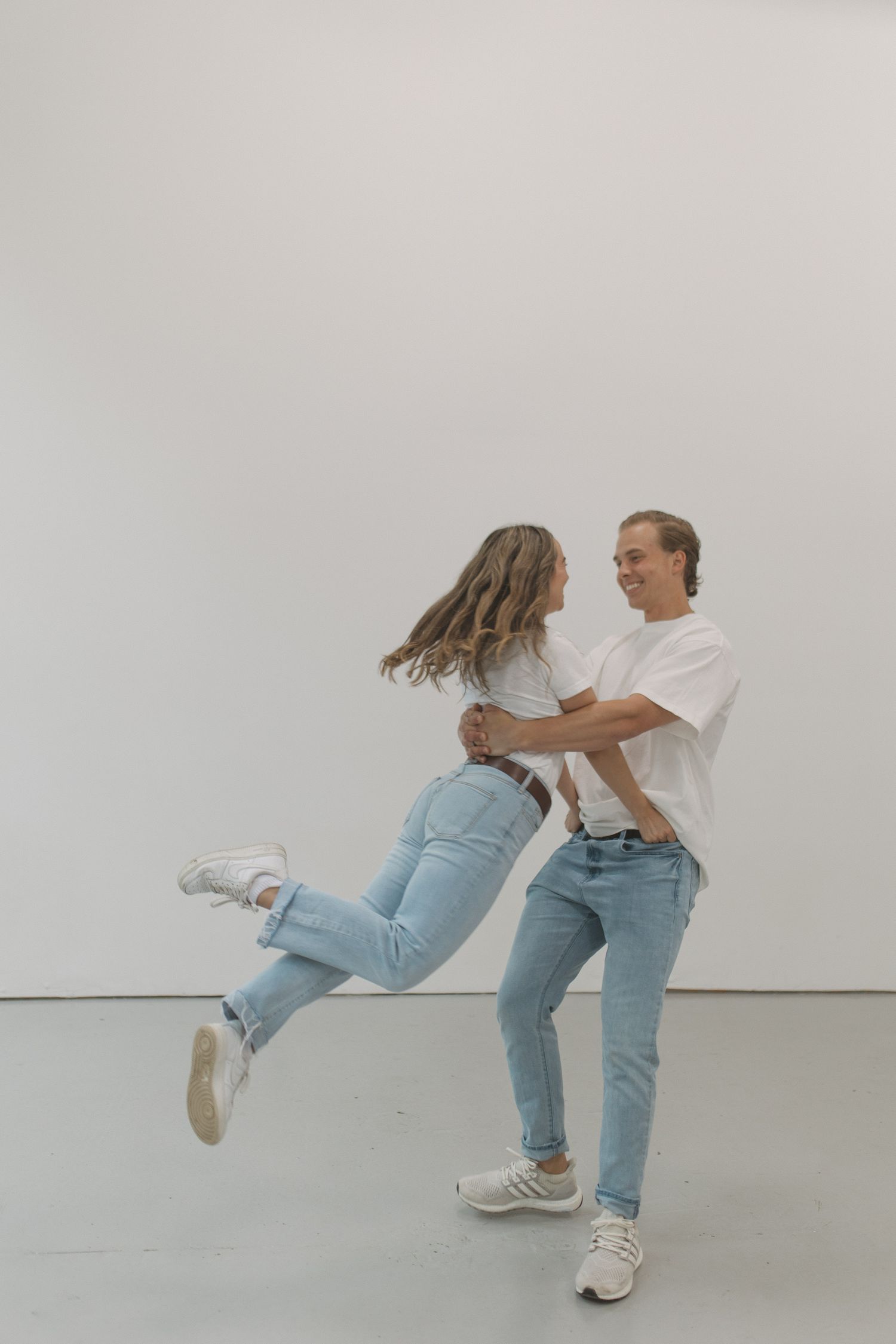 Joyful couple in matching white tees and jeans, man lifting woman as she jumps into his arms.