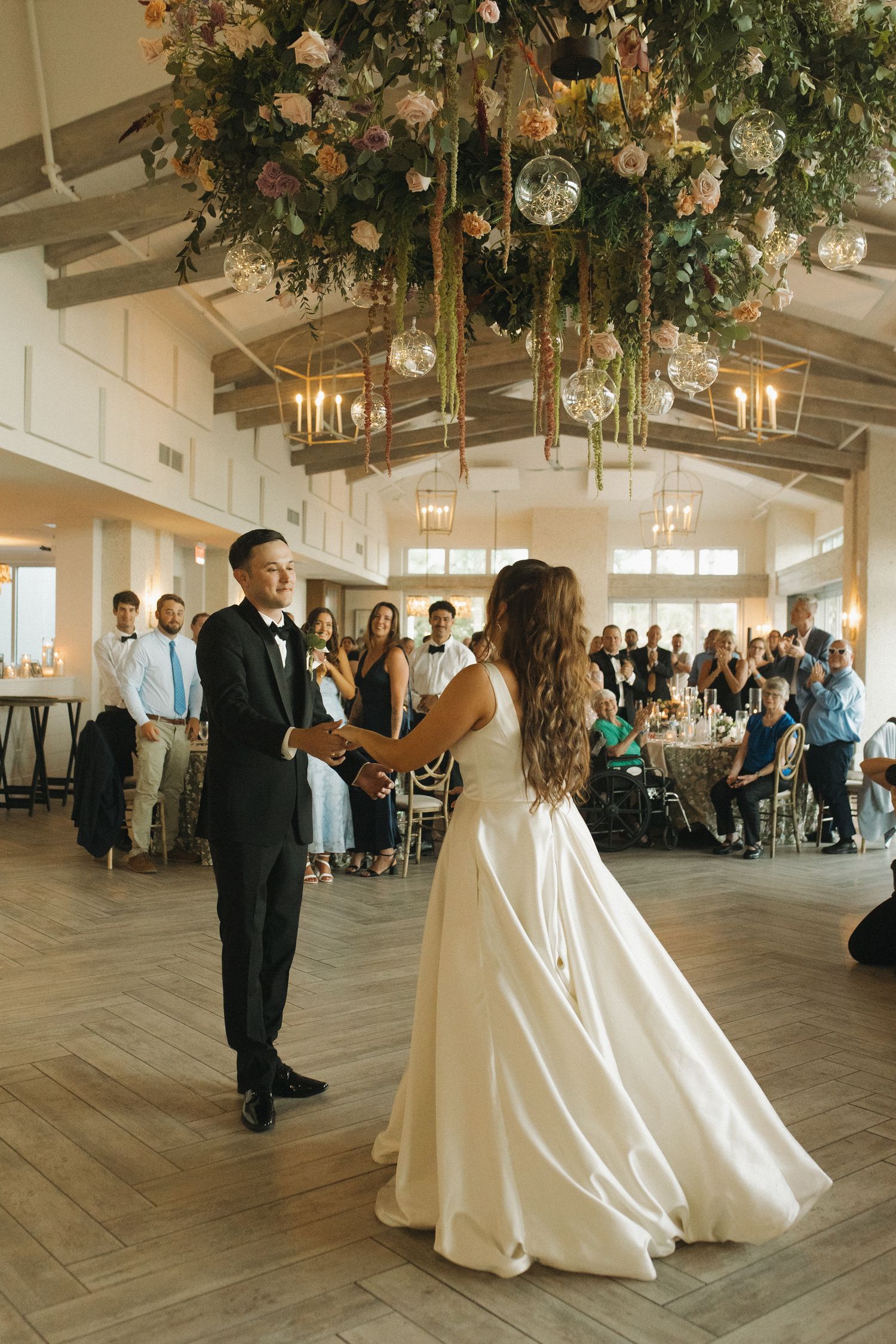 Bride and groom share their first dance under a floral chandelier at an elegant wedding reception.