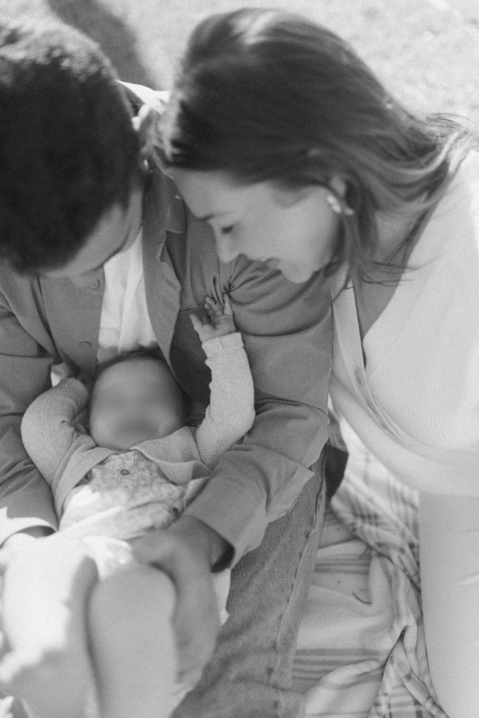 Black and white photo of parents lovingly gazing at their newborn baby held in fathers arms.