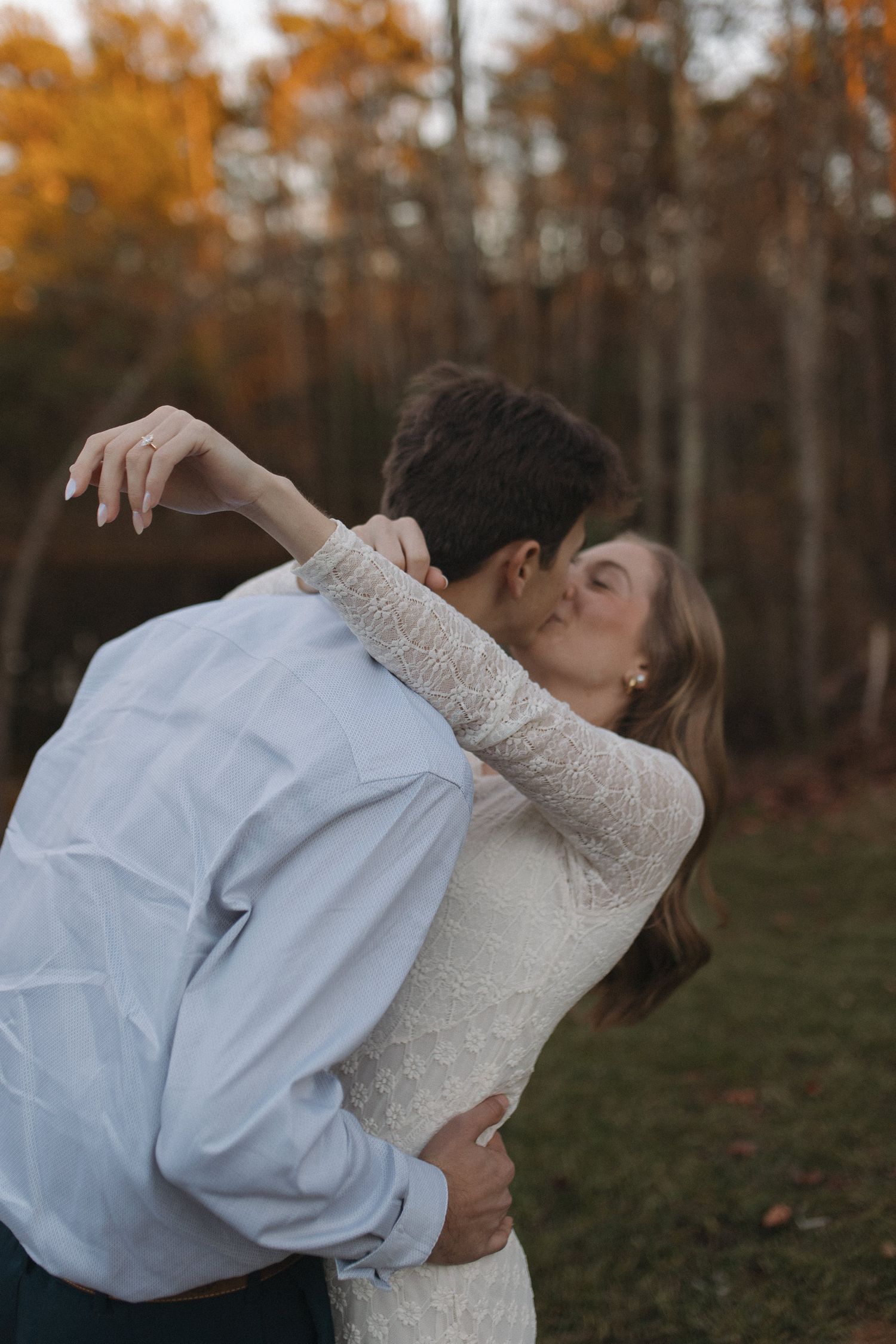 Engaged couple sharing a passionate kiss outdoors surrounded by colorful autumn foliage.