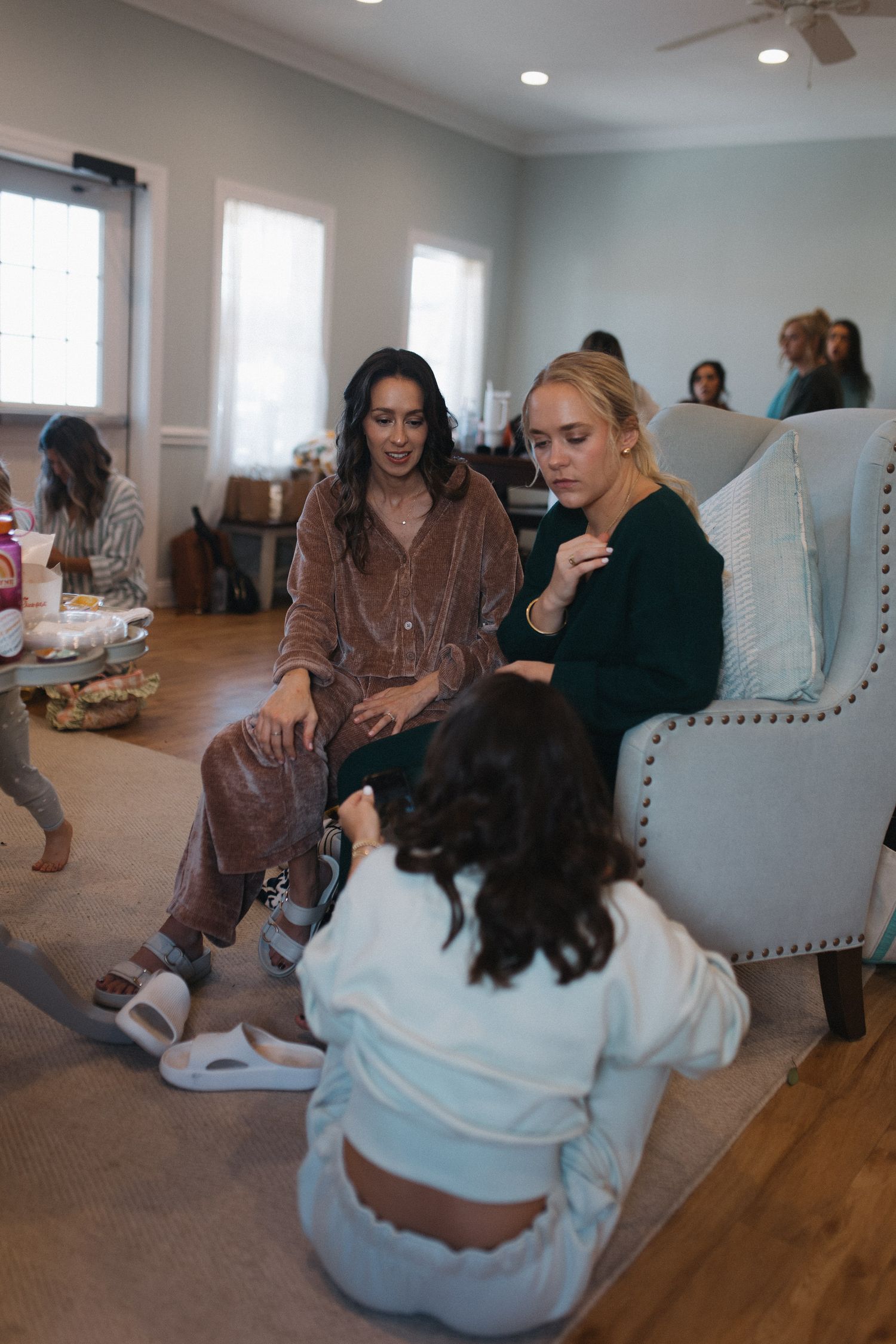 Women relaxing together in a cozy living room, sitting on chairs and floor during a casual indoor gathering.