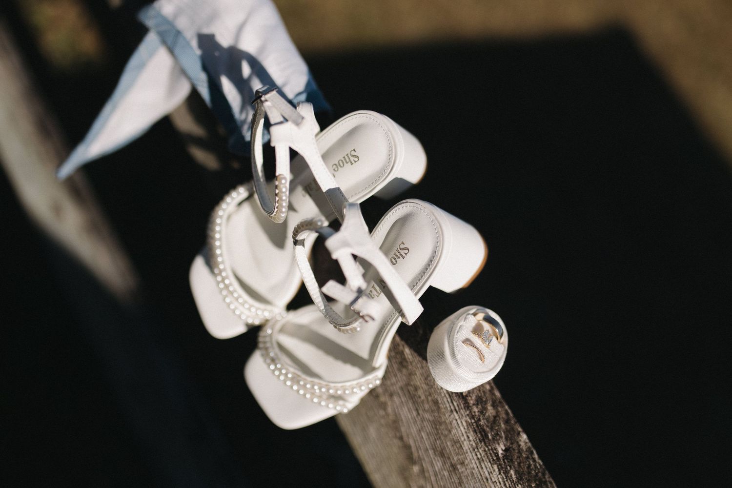Close-up of white wedding sandals with pearl details resting on a wooden surface.