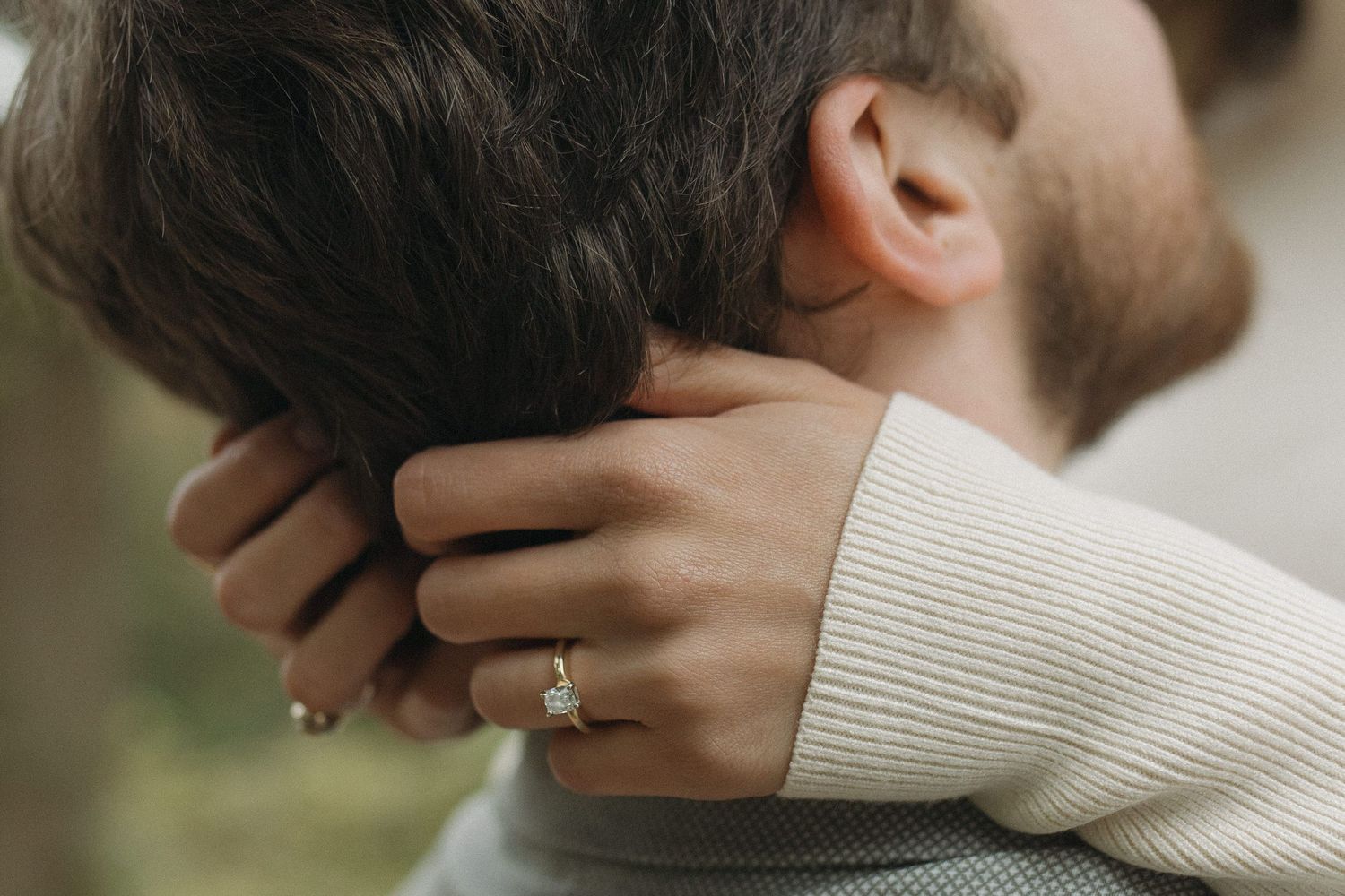 Close-up of woman with engagement ring embracing a man, hands wrapped around his neck.