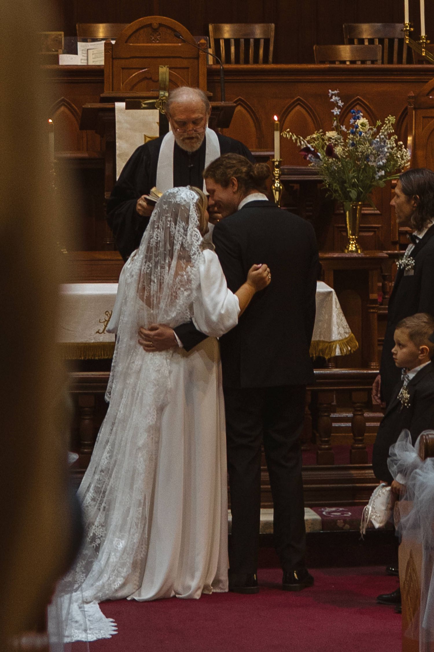Bride and groom sharing first kiss at church altar during wedding ceremony.